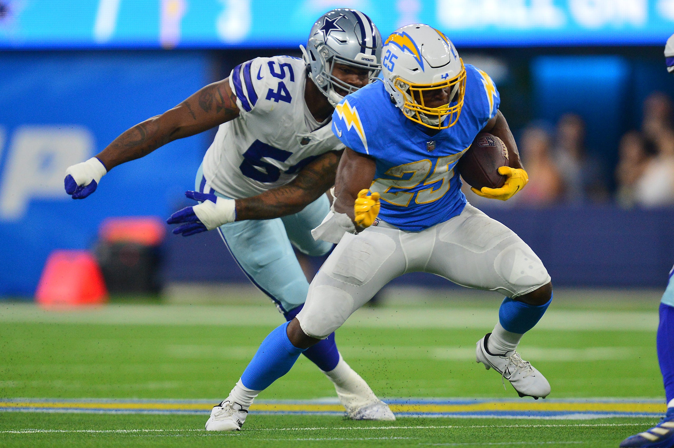Aug 20, 2022; Inglewood, California, USA; Los Angeles Chargers running back Joshua Kelley (25) runs the ball ahead of Dallas Cowboys defensive end Sam Williams (54) during the first half at SoFi Stadium. Mandatory Credit: Gary A. Vasquez-USA TODAY Sports