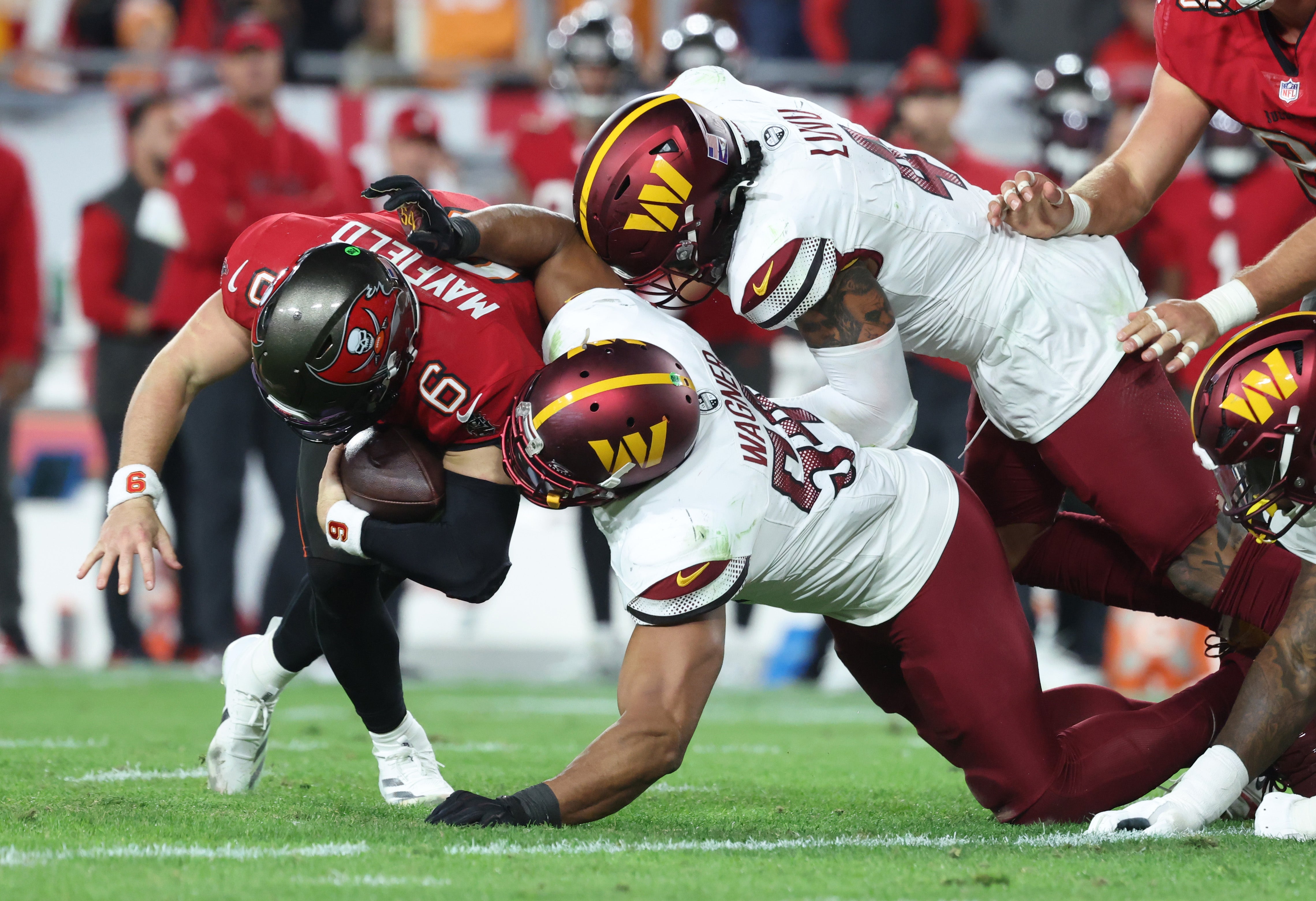 Jan 12, 2025; Tampa, Florida, USA; Tampa Bay Buccaneers quarterback Baker Mayfield (6) is tackled by Washington Commanders linebacker Bobby Wagner (54) and linebacker Dante Fowler Jr. (6) during the fourth quarter of a NFC wild card playoff at Raymond James Stadium.