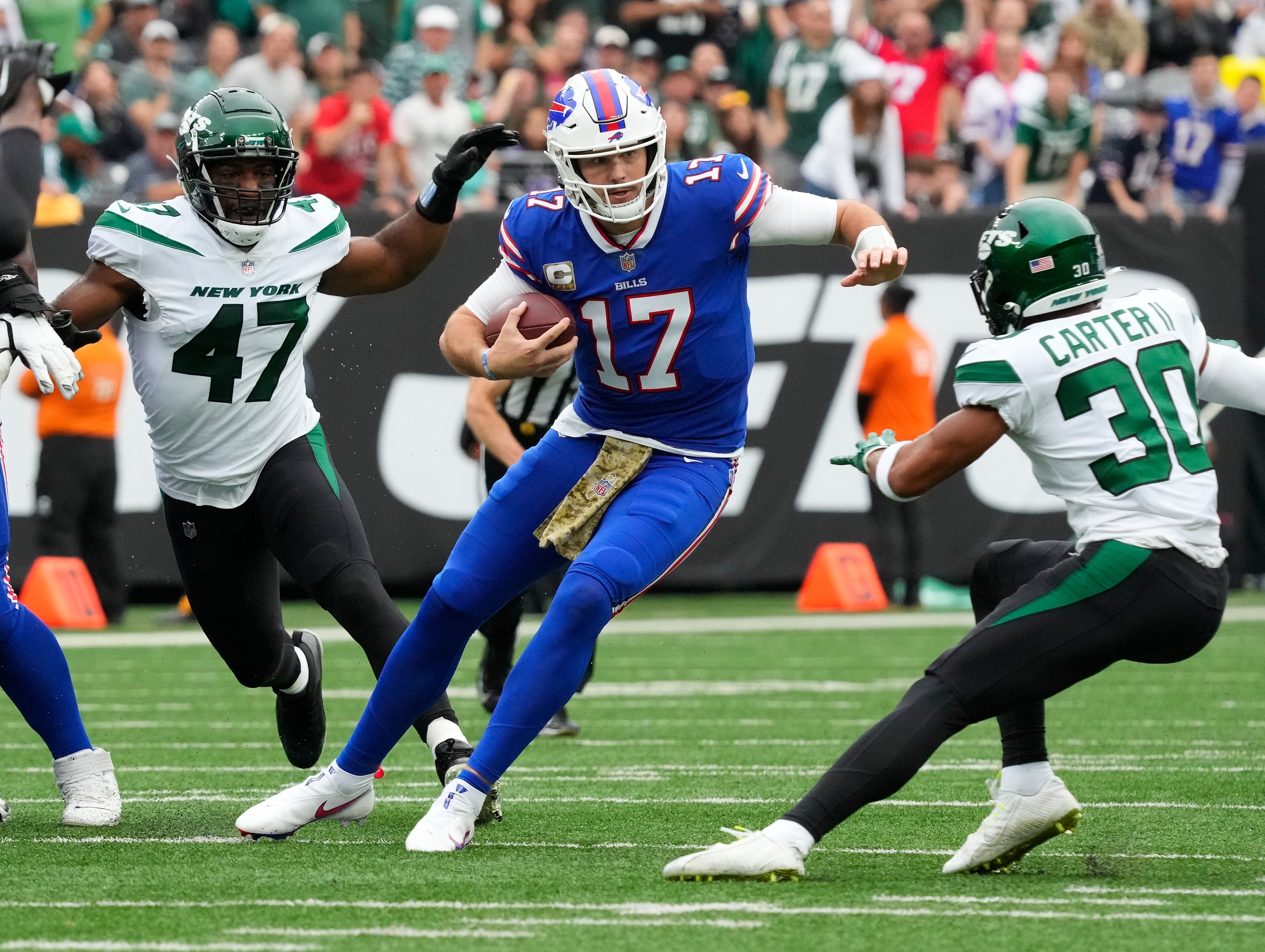 uffalo Bills quarterback Josh Allen (17) runs in the first half as New York Jets players Bryce Huff (47) and Michael Carter II (30) defend at MetLife Stadium.