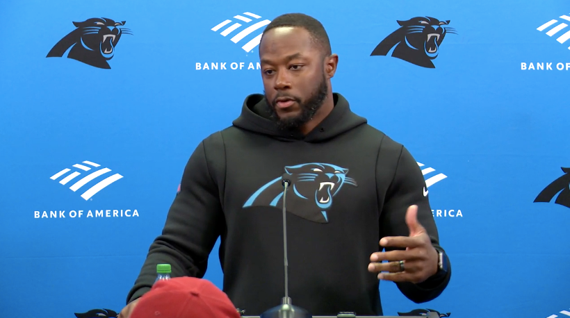 Thomas Brown speaks with media following his promotion to lead offensive play caller. He wears a black hoodie with the Panthers' blue and black logo. Feature image via Panthers.com.