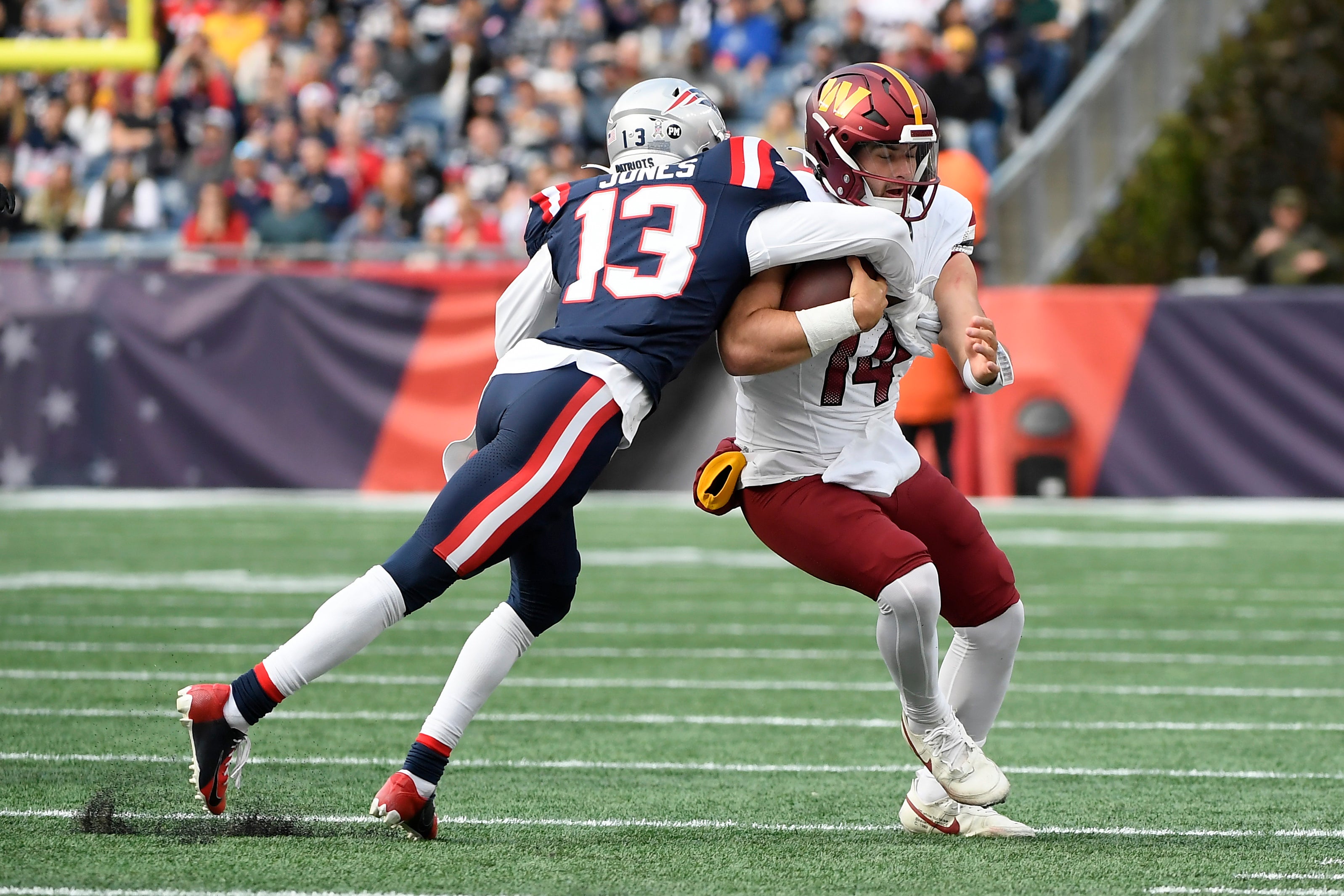 Washington Commanders quarterback Sam Howell gets tackled by New England Patriots cornerback Jack Jones
