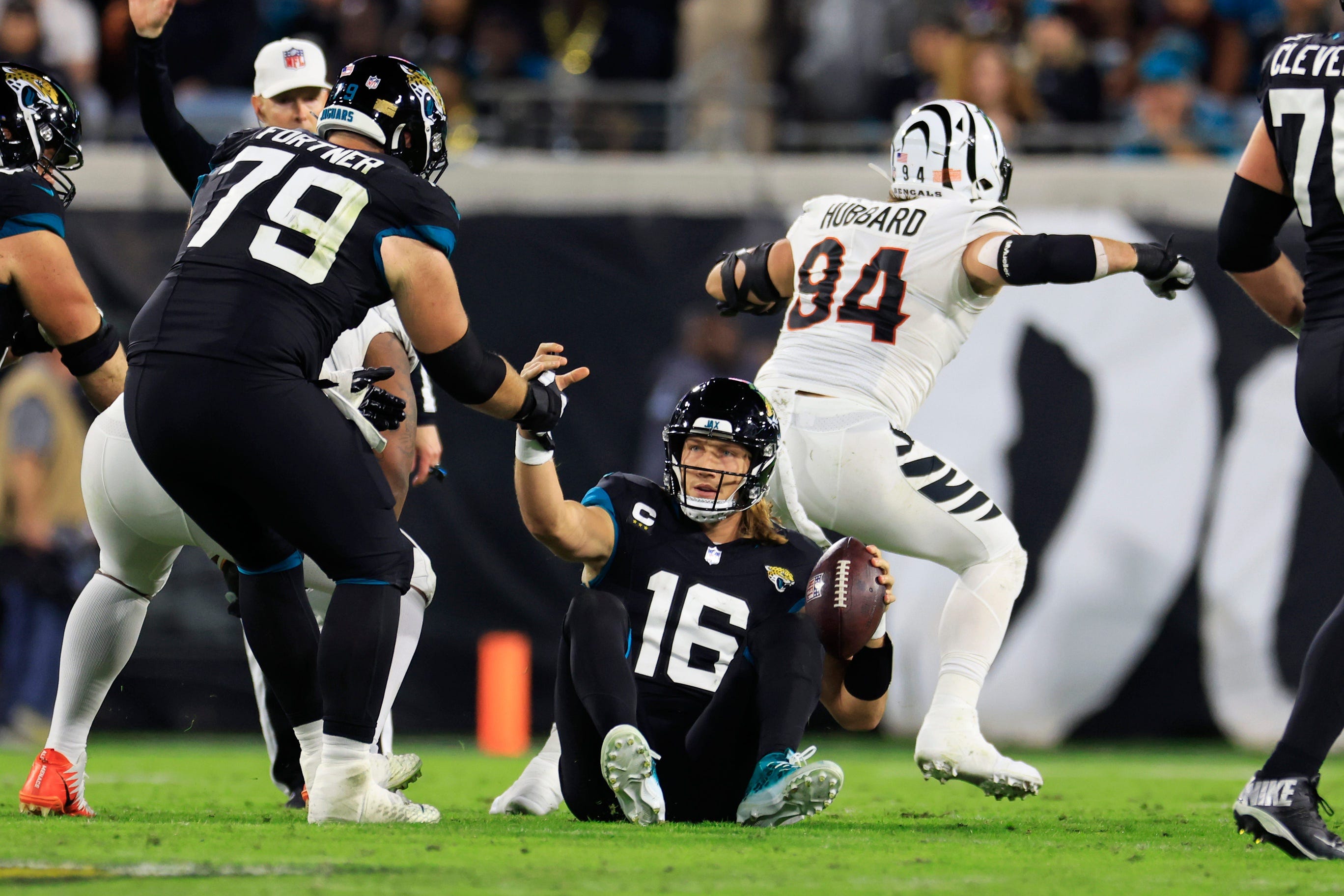 Jacksonville Jaguars quarterback Trevor Lawrence (16) is helped up by center Luke Fortner (79) after being sacked by Cincinnati Bengals defensive end Sam Hubbard (94) during the second quarter of a regular season NFL football matchup Monday, Dec. 4, 2023 at EverBank Stadium in Jacksonville, Fla. The Cincinnati Bengals defeated the Jacksonville Jaguars 34-31 in overtime.