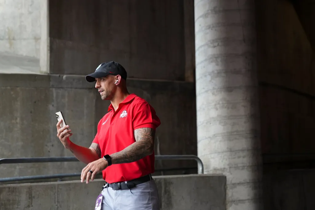 Ohio State Buckeyes assitant coach James Laurinaitis talks on the phone as he heads to the field prior to the NCAA football game against the Western Kentucky Hilltoppers.