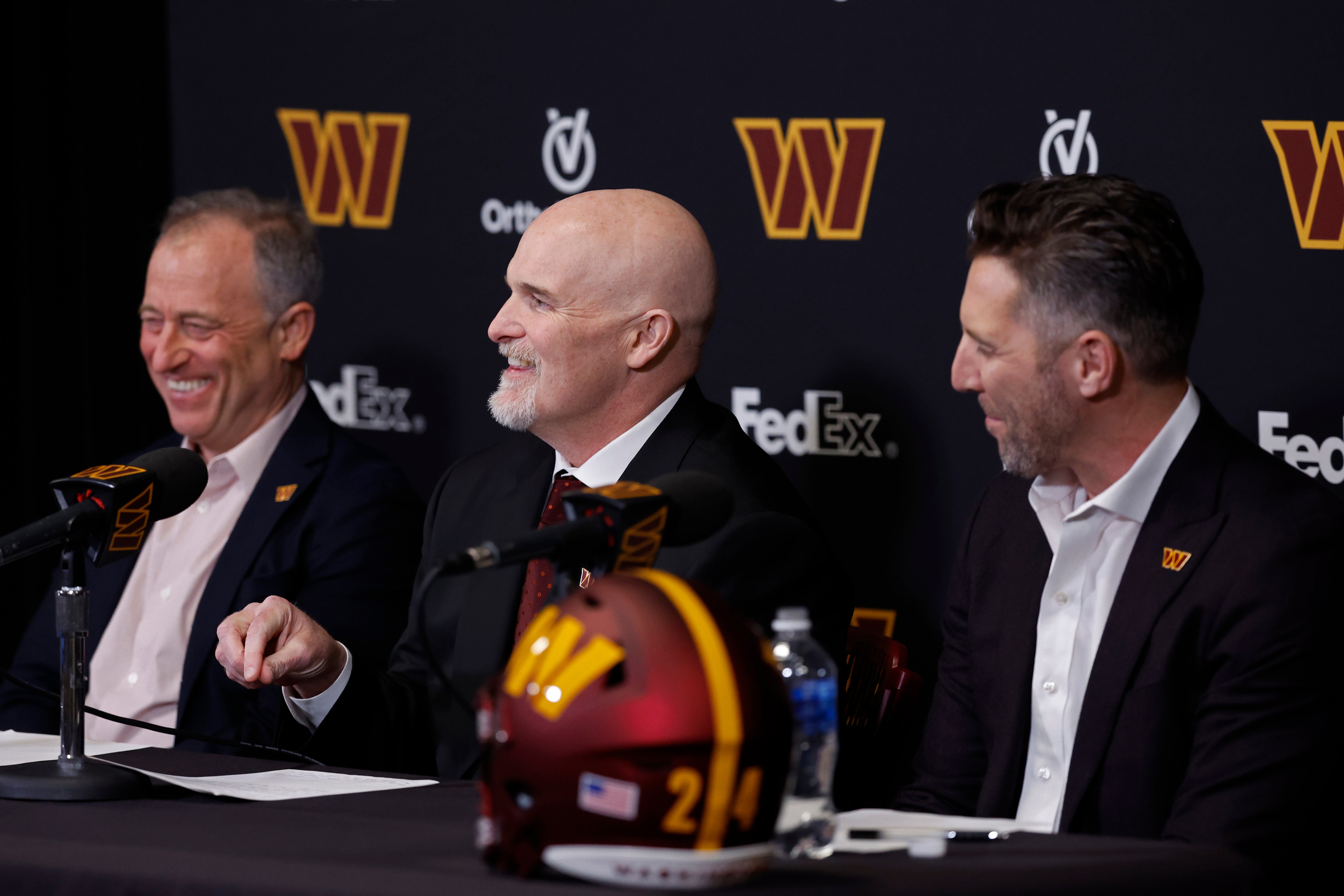 Washington Commanders majority owner Josh Harris (L) and Commanders general manager Adam Peters (R) laugh as Commanders head coach Dan Quinn (R) speaks during his introductory press conference at Commanders Park.