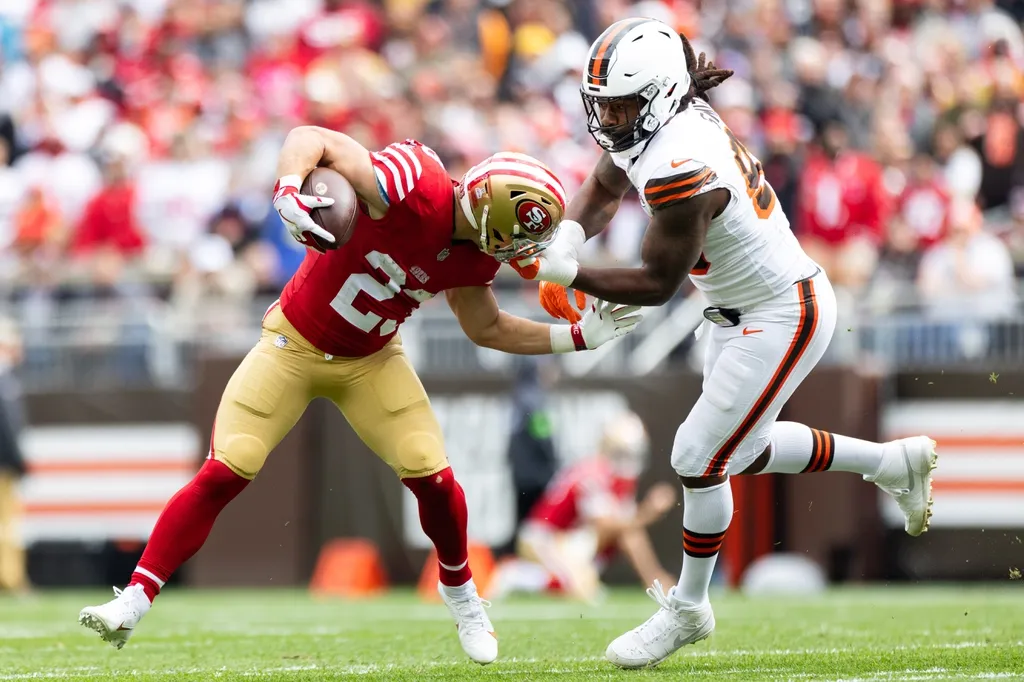 San Francisco 49ers running back Christian McCaffrey (23) runs the ball as Cleveland Browns defensive end Za'Darius Smith (99) grabs him by the face mask during the first quarter at Cleveland Browns Stadium.