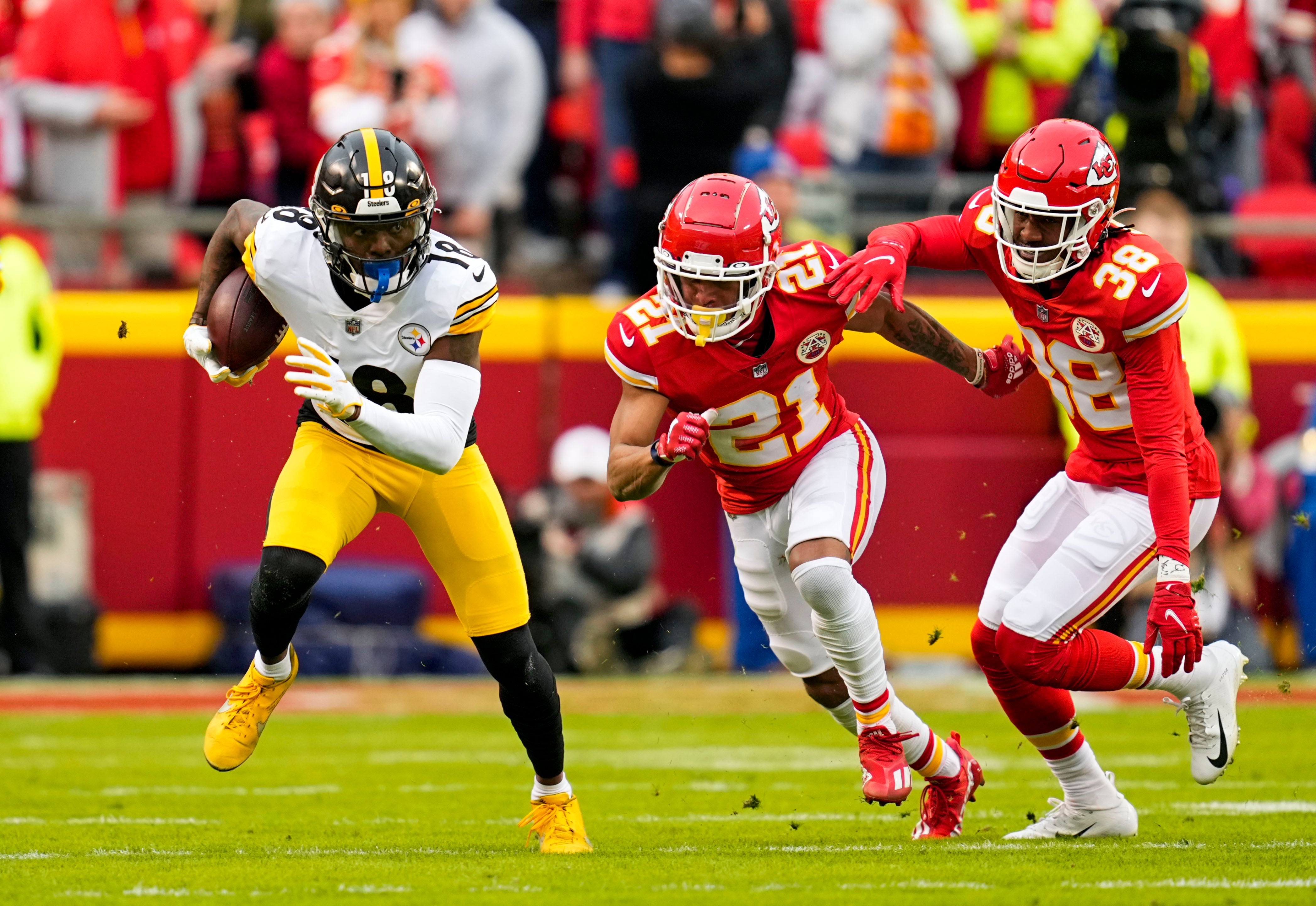 Dec 26, 2021; Kansas City, Missouri, USA; Pittsburgh Steelers wide receiver Diontae Johnson (18) runs the ball against Kansas City Chiefs cornerback Mike Hughes (21) and cornerback L'Jarius Sneed (38) during the first half at GEHA Field at Arrowhead Stadium. Mandatory Credit: Jay Biggerstaff-USA TODAY Sports