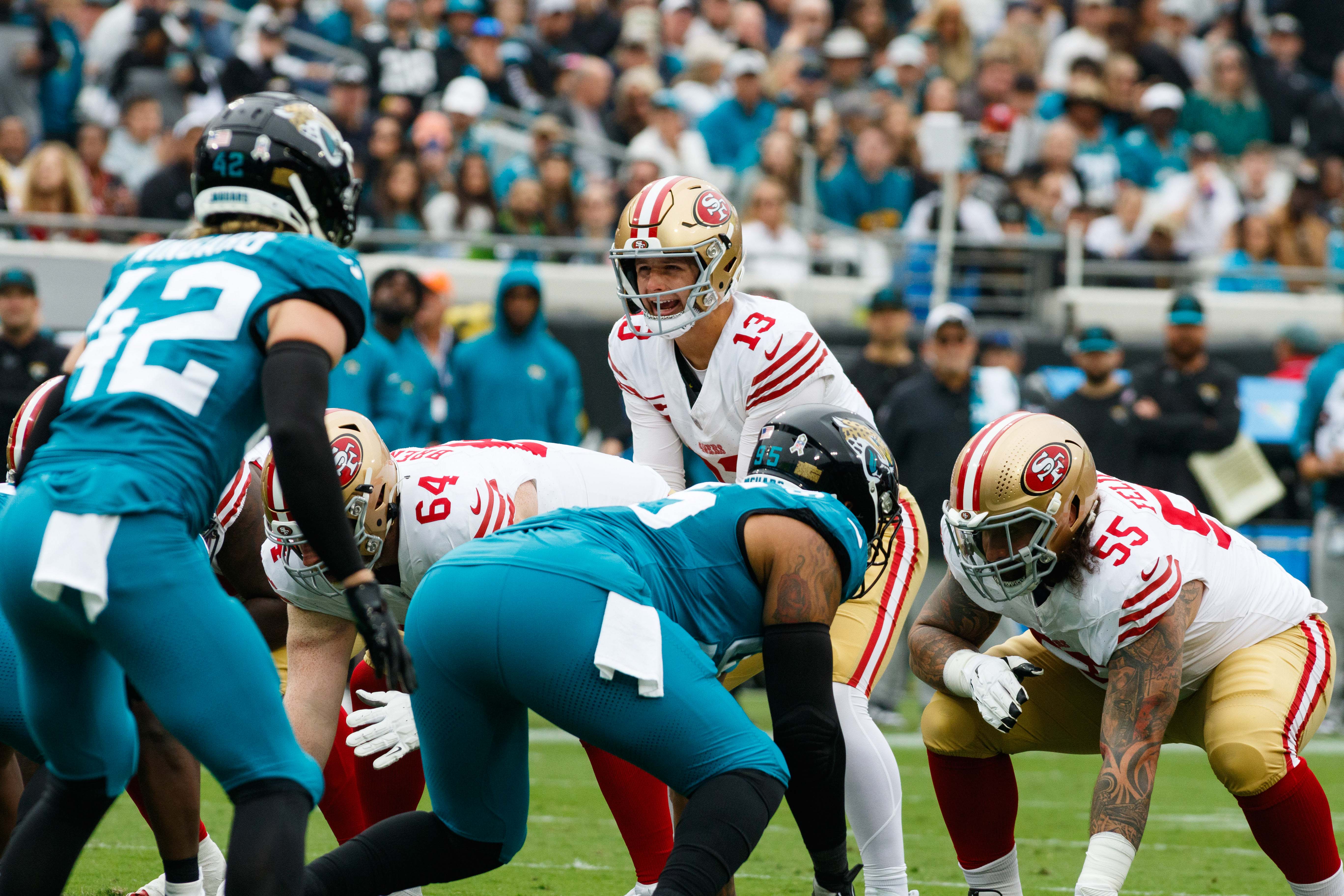 Nov 12, 2023; Jacksonville, Florida, USA; San Francisco 49ers quarterback Brock Purdy (13) calls a play guarded by offensive tackle Jake Brendel (64) and offensive tackle Jon Feliciano (55) with Jacksonville Jaguars safety Andrew Wingard (42) and defensive lineman Roy Robertson-Harris (95) lined up during the first quarter at EverBank Stadium.