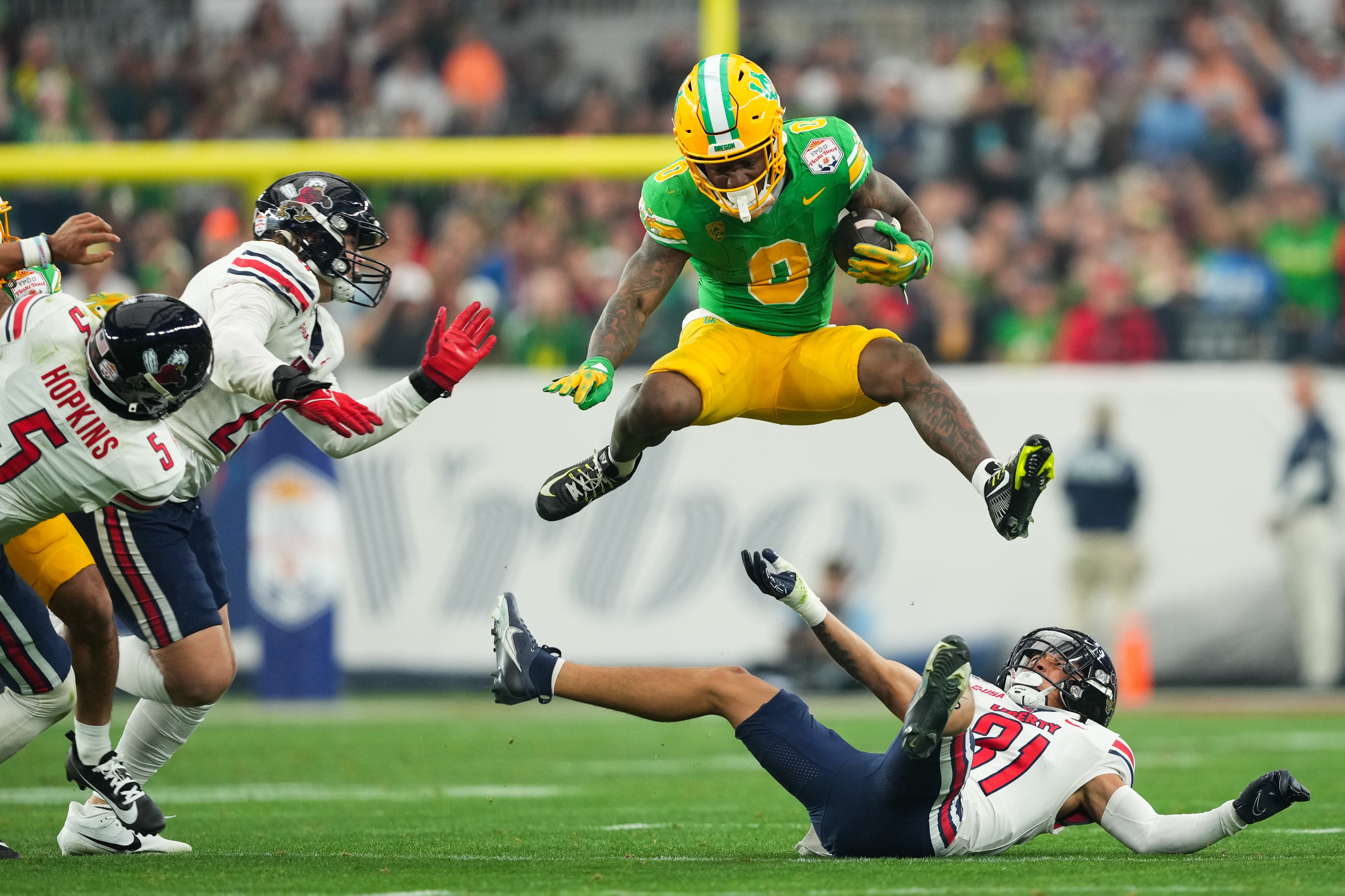 Jan 1, 2024; Glendale, AZ, USA; Oregon Ducks running back Bucky Irving (0) hurdles over Liberty Flames defensive back Brandon Bishop (6) during the second half in the 2024 Fiesta Bowl at State Farm Stadium.