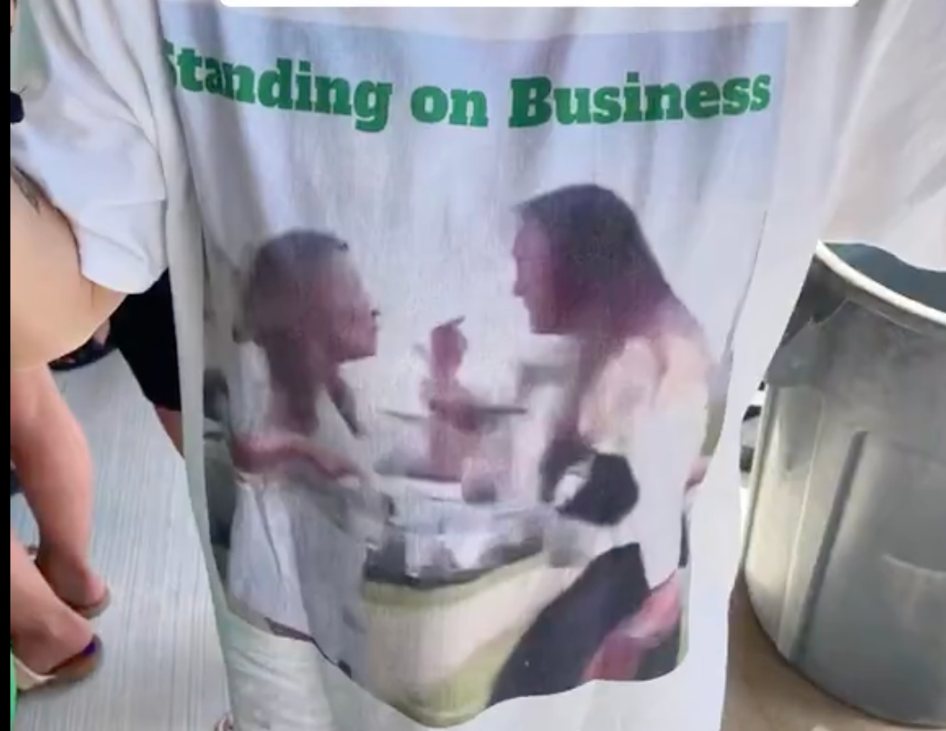 Fans wear a shirt showing Kylie Kelce standing up to a crazy fan at the 2024 New Heights Beer Bowl, captioned "Standing on Business."