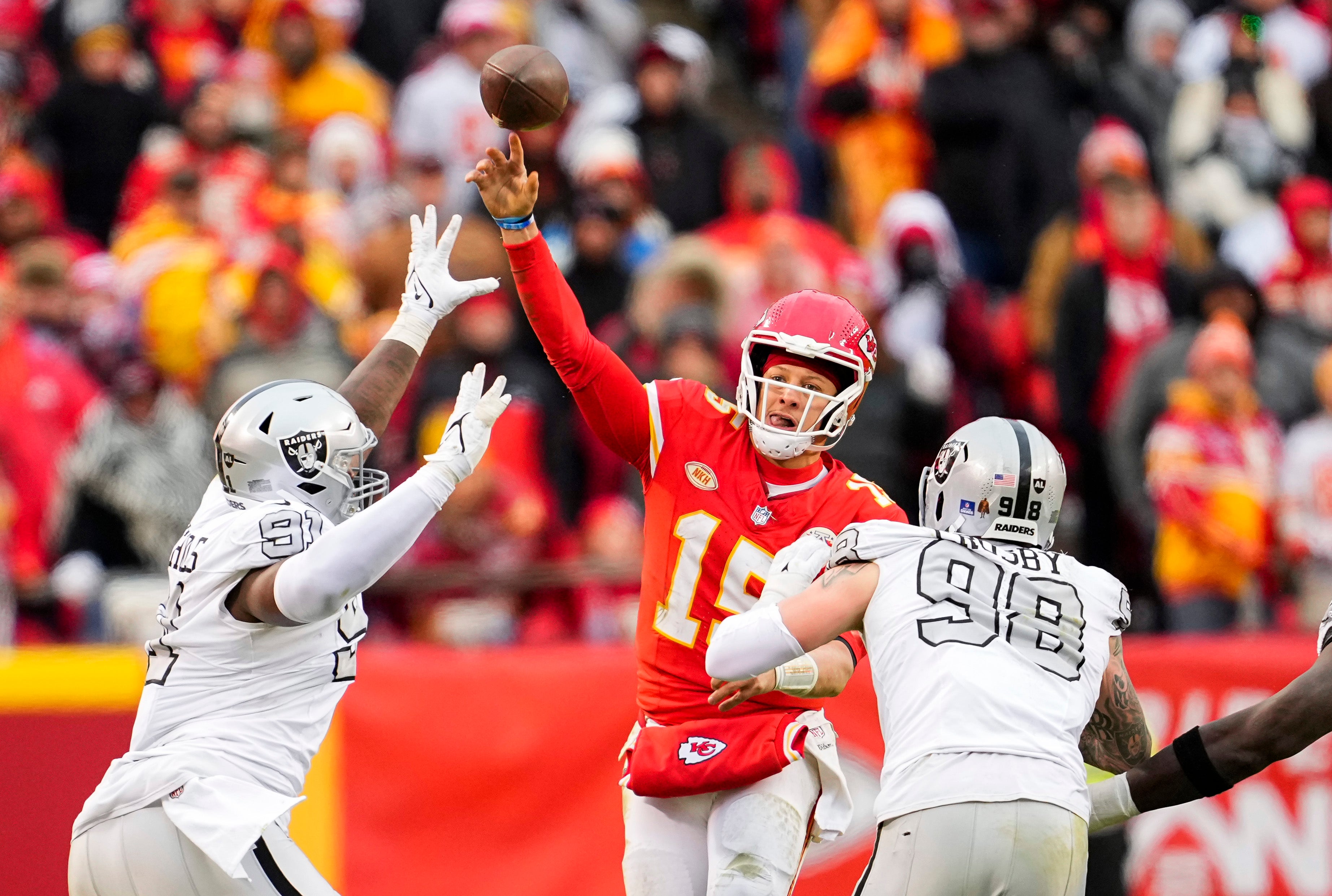 Chiefs QB Patrick Mahomes throws a pass under pressure from Raiders' defense.