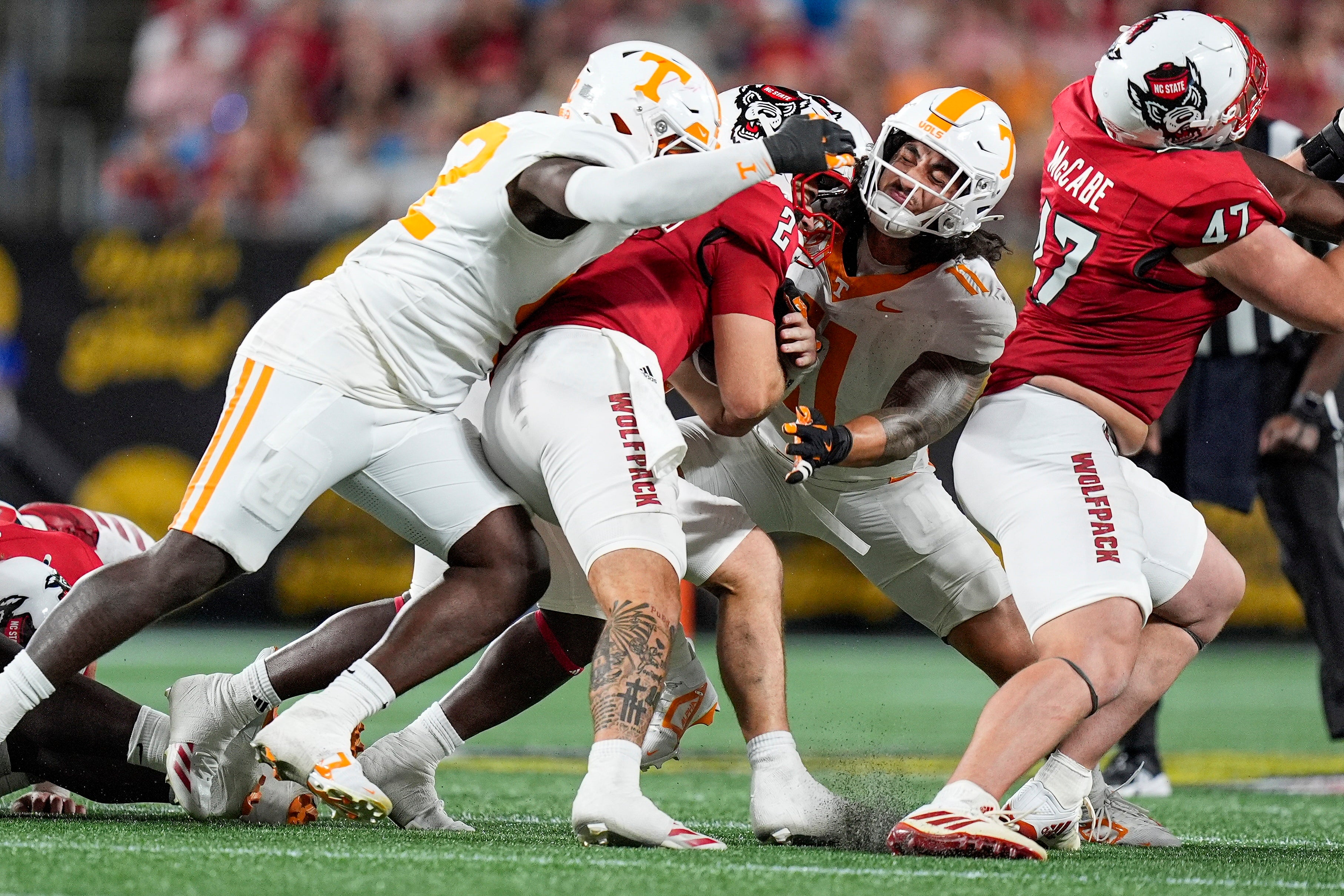 Sep 7, 2024; Charlotte, North Carolina, USA; North Carolina State Wolfpack quarterback Grayson McCall (2) is tackled by Tennessee Volunteers linebacker Keenan Pili (11) and linebacker Eli Purcell (52) during the second half at the Dukes Mayo Classic at Bank of America Stadium.