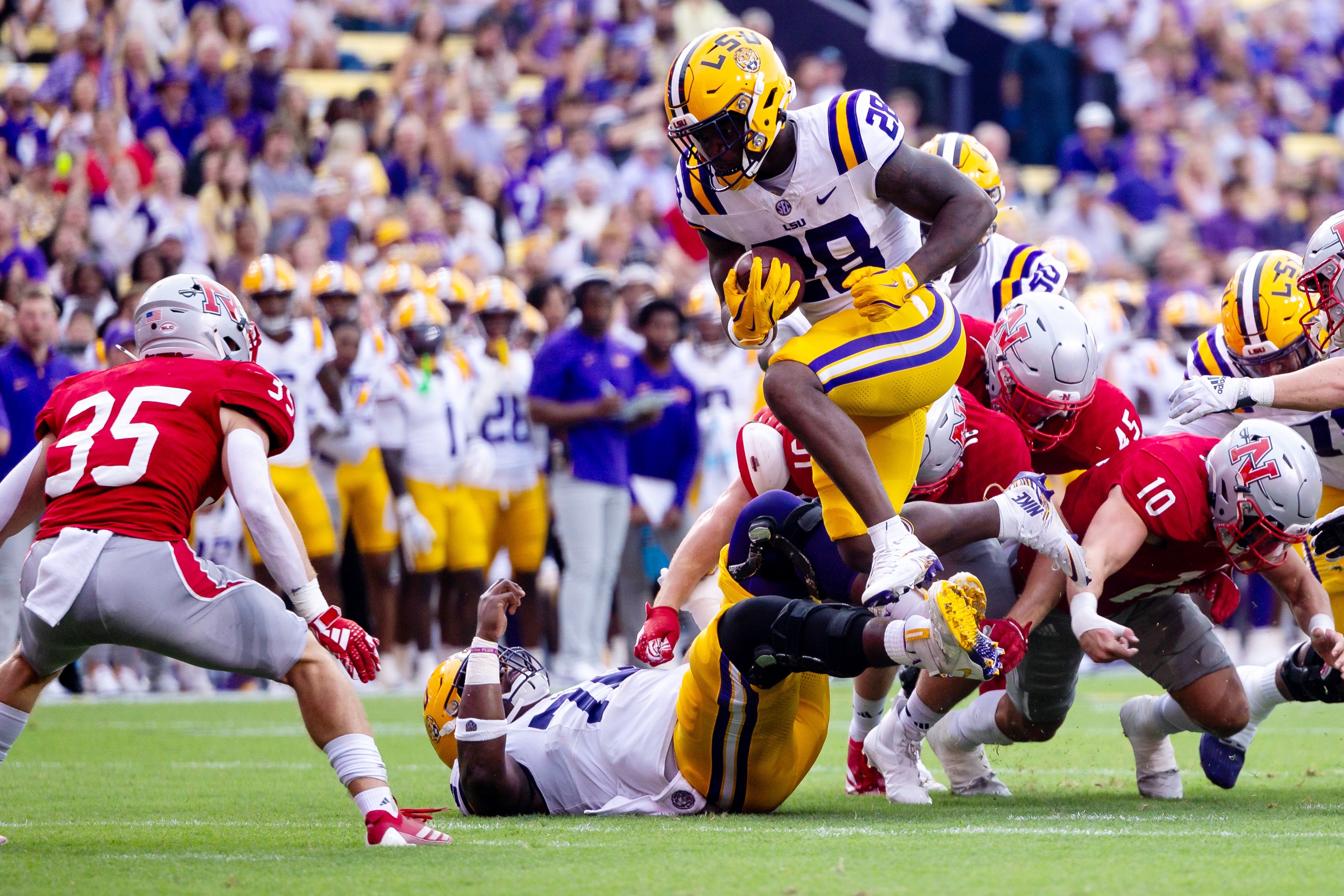 Sep 7, 2024; Baton Rouge, Louisiana, USA; LSU Tigers running back Kaleb Jackson (28) leaps over Nicholls State Colonels linebacker Hayden Shaheen (10) and is tackled by defensive back Ethan Lee (35) during the first half at Tiger Stadium.