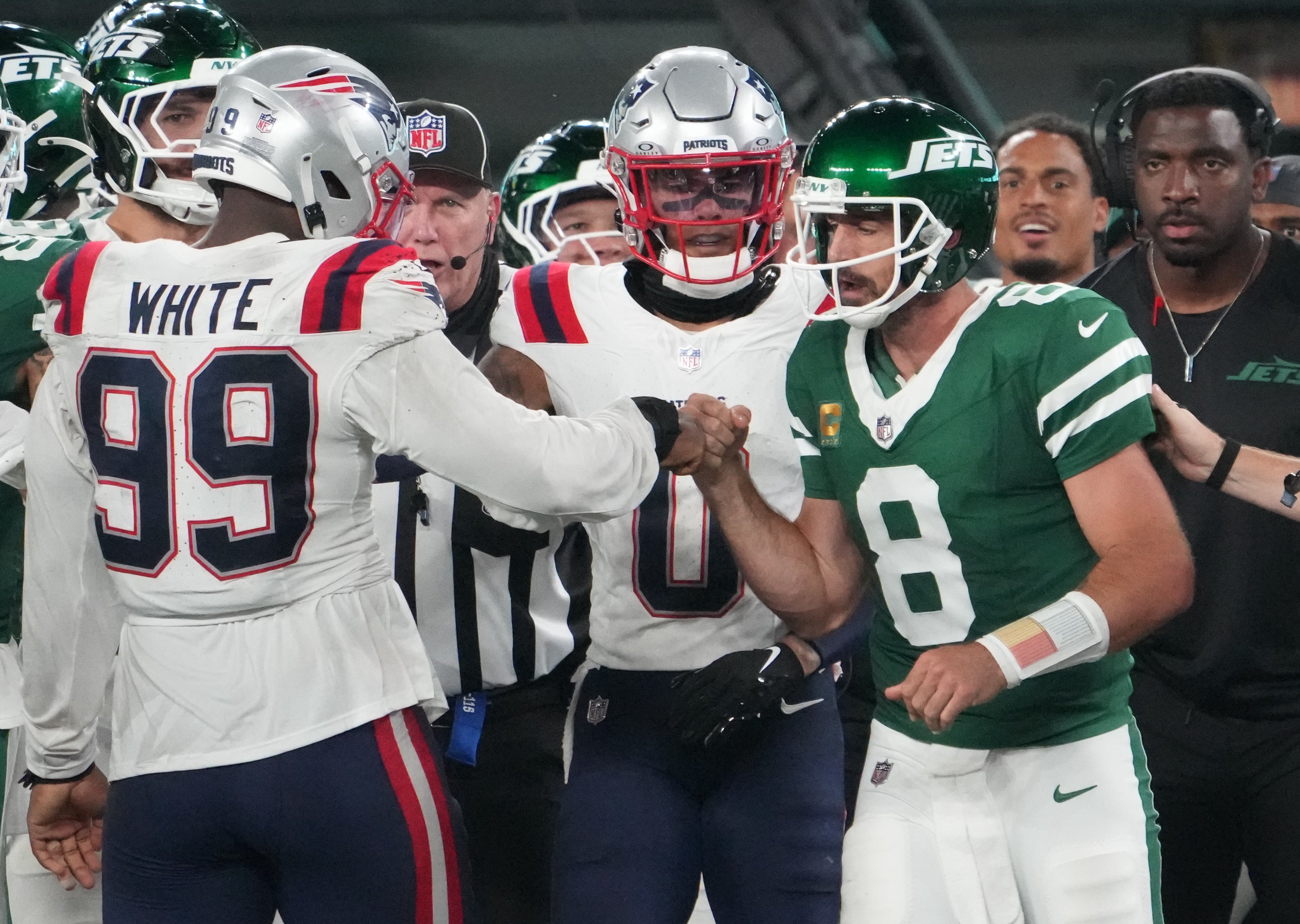 Sep 19, 2024; East Rutherford, New Jersey, USA; New York Jets quarterback Aaron Rodgers (8) bumps fists with New England Patriots defensive end Keion White (99) after Rogers was tackled on the sidelines by White in the second half at MetLife Stadium.