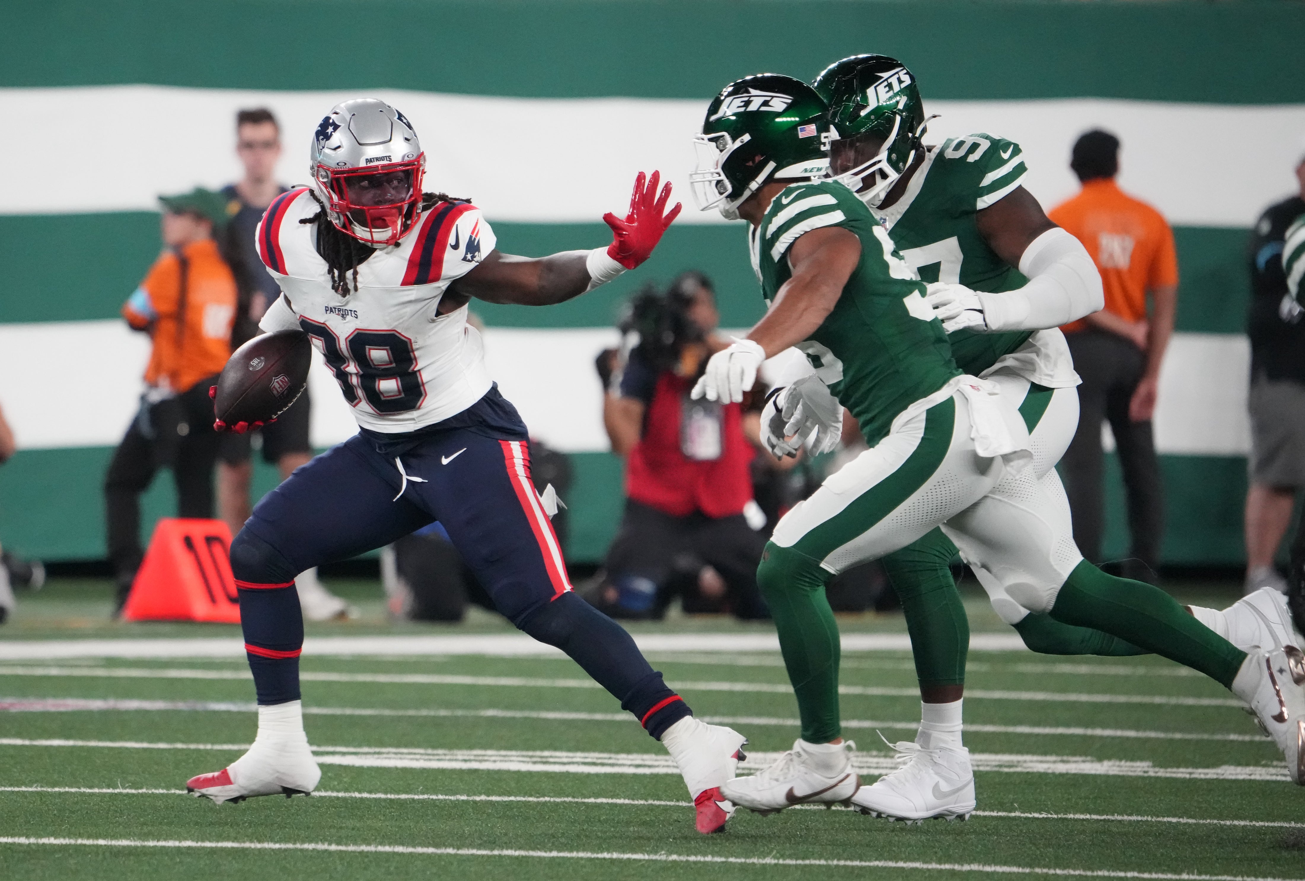 Sep 19, 2024; East Rutherford, New Jersey, USA; New England Patriots running back Rhamondre Stevenson (38) runs away from New York Jets linebacker Chazz Surratt (55) and defensive end Jalyn Holmes (97) at MetLife Stadium.