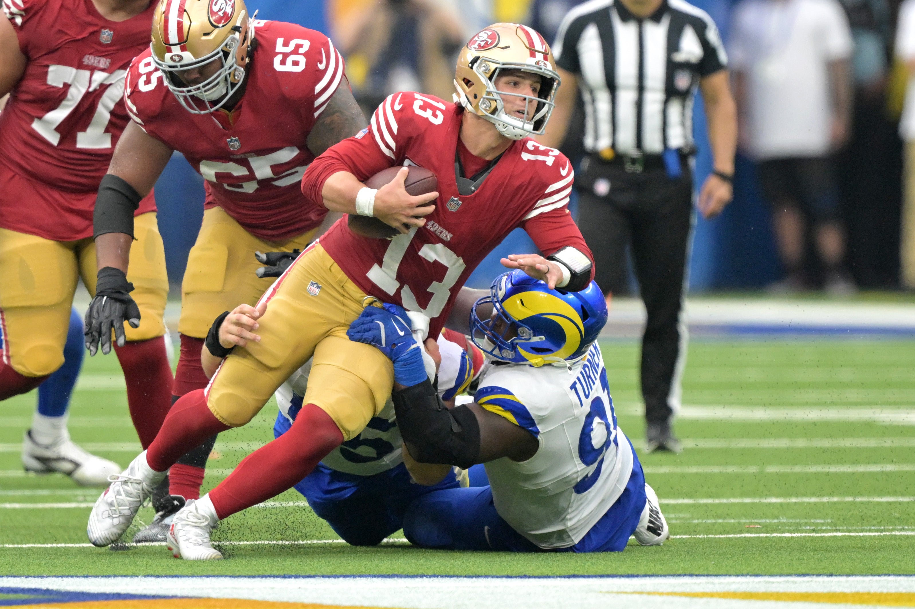 San Francisco 49ers quarterback Brock Purdy (13) is stopped by Los Angeles Rams defensive tackle Braden Fiske (55) and defensive tackle Kobie Turner (91) for a first down in the second half at SoFi Stadium.