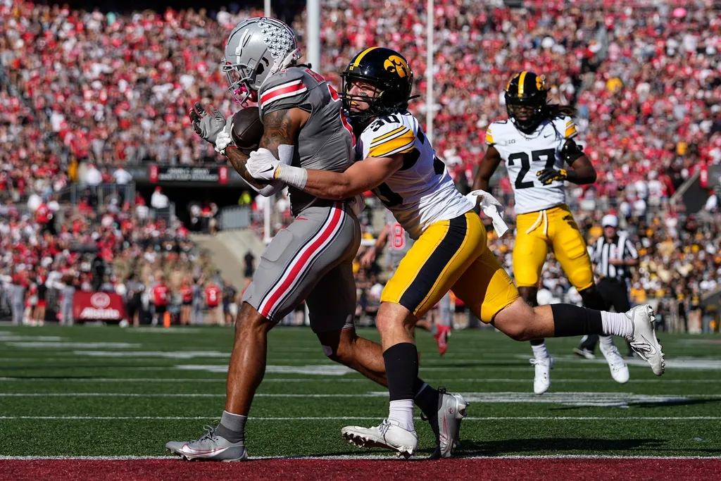 Ohio State Buckeyes wide receiver Emeka Egbuka (2) catches a touchdown pass as he's hit by Iowa Hawkeyes defensive back Quinn Schulte (30) during the first half of the NCAA football game at Ohio Stadium.