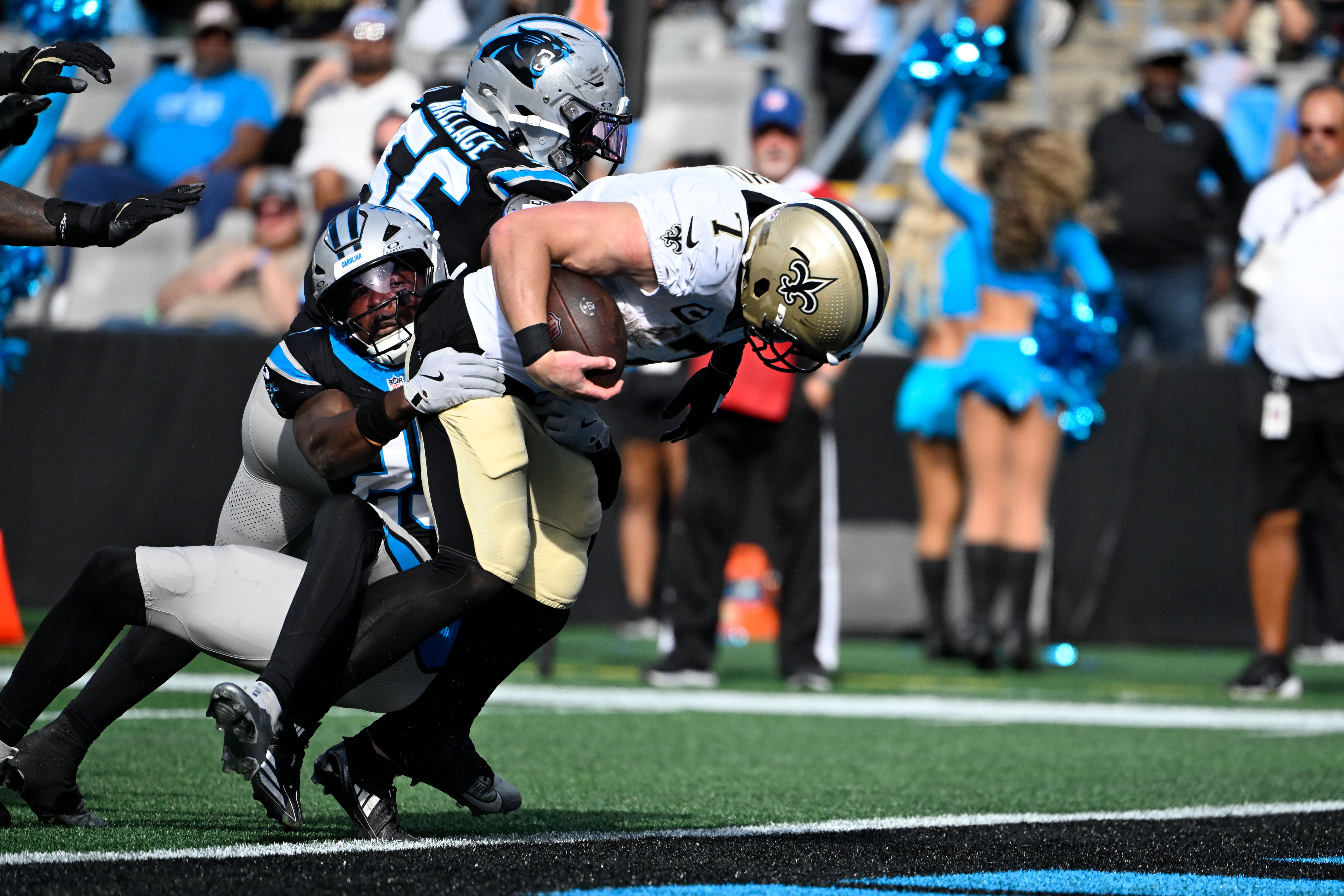Saints tight end Taysom Hill (7) scores a touchdown as Carolina Panthers safety Xavier Woods (25) and linebacker Trevin Wallace (56) defend.