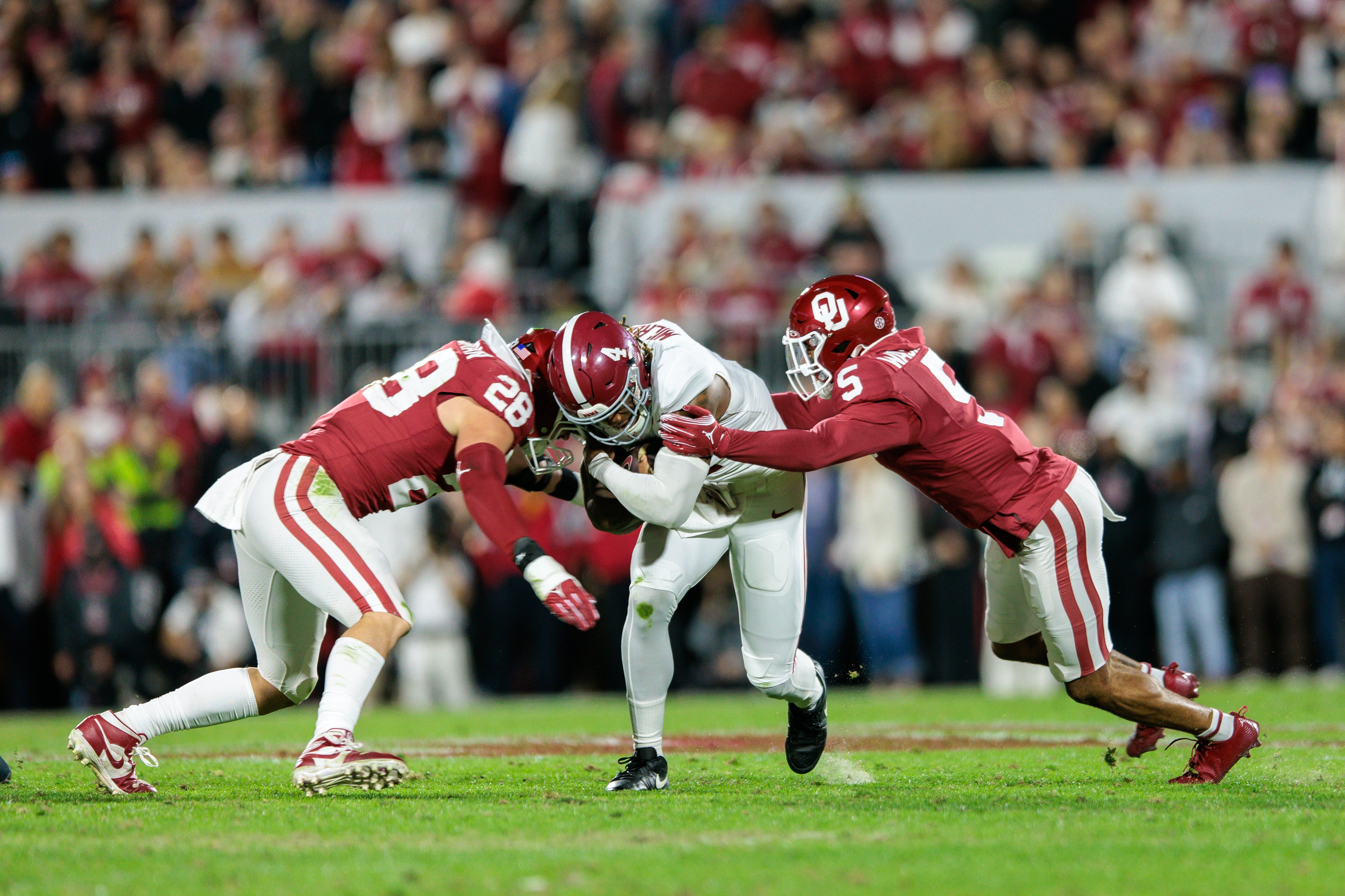 Nov 23, 2024; Norman, Oklahoma, USA; Alabama Crimson Tide quarterback Jalen Milroe (4) is hit by Oklahoma Sooners linebacker Danny Stutsman (28) and defensive back Woodi Washington (5) during the first quarter at Gaylord Family-Oklahoma Memorial Stadium.