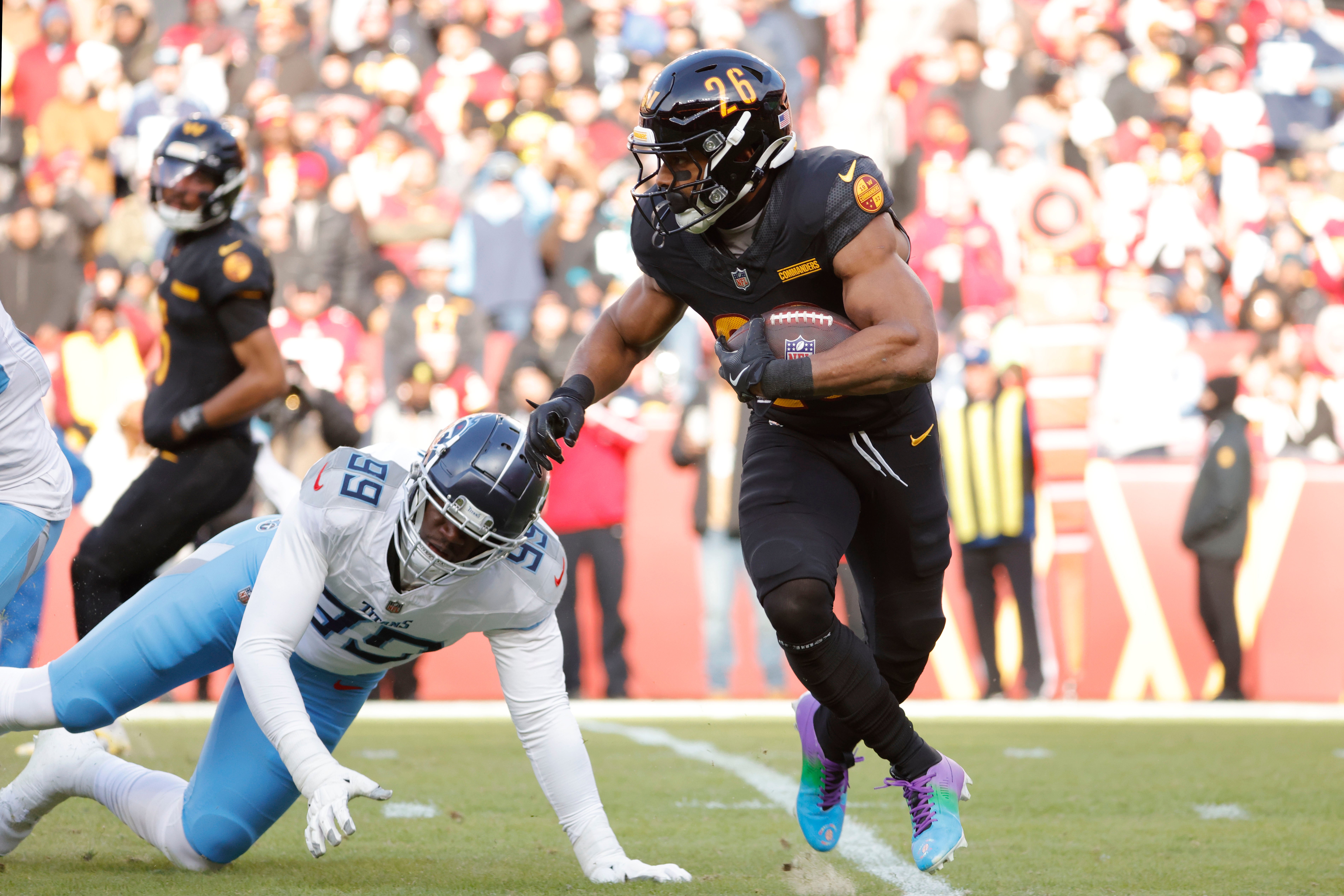 Dec 1, 2024; Landover, Maryland, USA; Washington Commanders running back Jeremy McNichols (26) carries the ball past Tennessee Titans linebacker Ali Gaye (99) during the first half at Northwest Stadium. Mandatory Credit: Amber Searls-Imagn Images