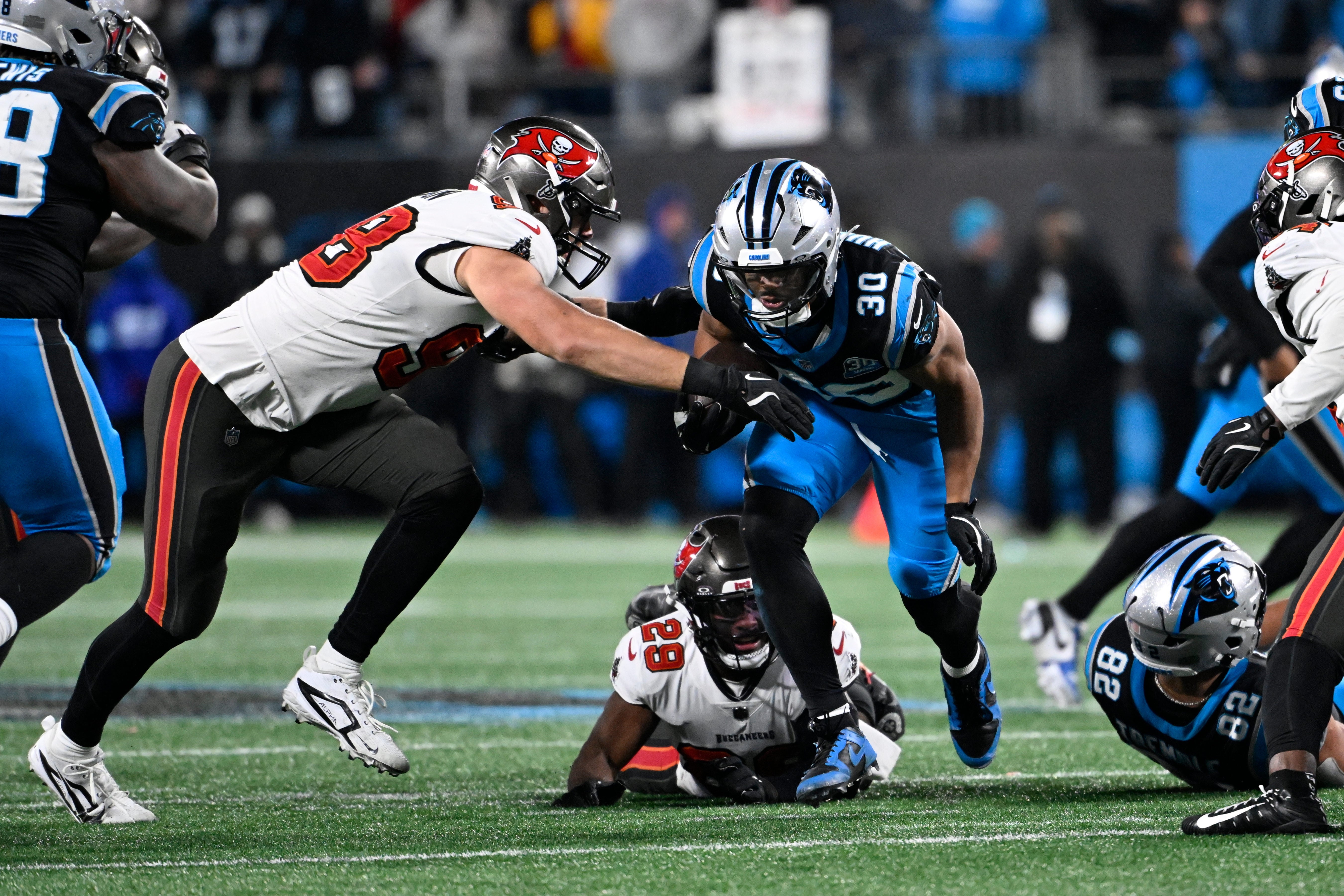 Dec 1, 2024; Charlotte, North Carolina, USA; Tampa Bay Buccaneers linebacker Anthony Nelson (98) strips Carolina Panthers running back Chuba Hubbard (30) of the ball as safety Christian Izien (29) helps defend in overtime at Bank of America Stadium.