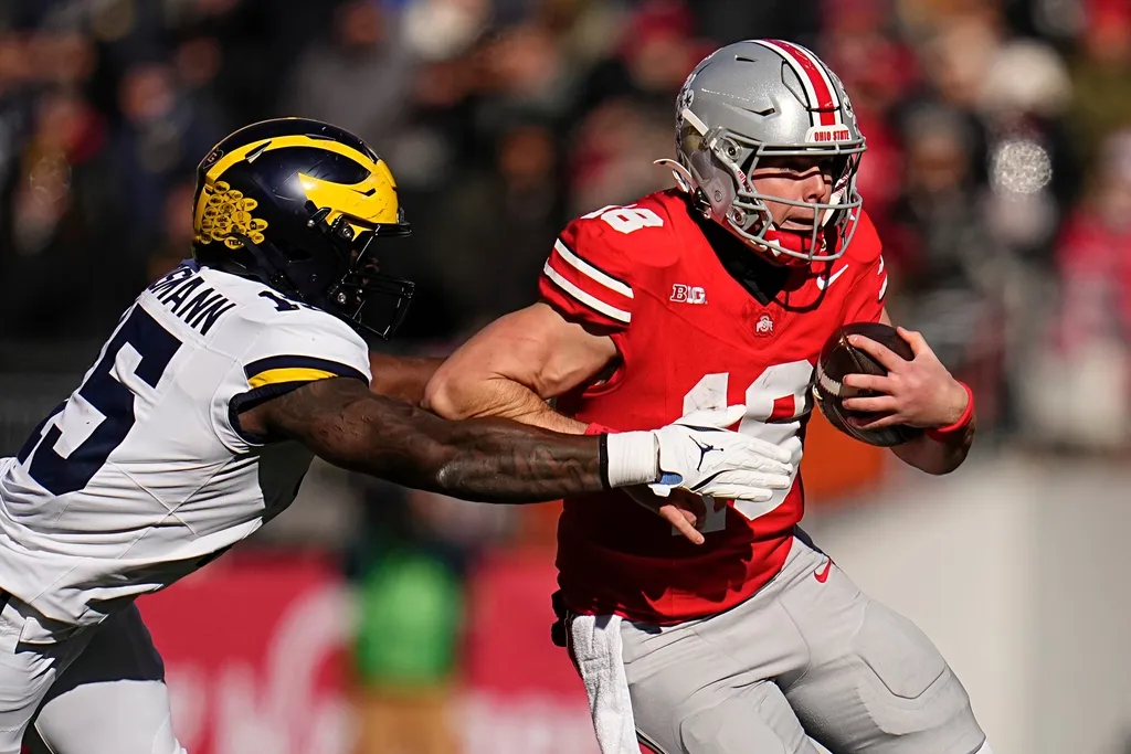 Ohio State Buckeyes quarterback Will Howard (18) runs past Michigan Wolverines linebacker Ernest Hausmann (15) during the NCAA football game at Ohio Stadium in Columbus on Tuesday, Dec. 3, 2024.