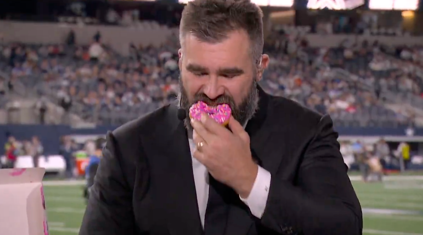 Jason Kelce takes a bite of a donut and then signs it for a fan prior to the Monday Night football game between the Dallas Cowboys and the Cincinnati Bengals