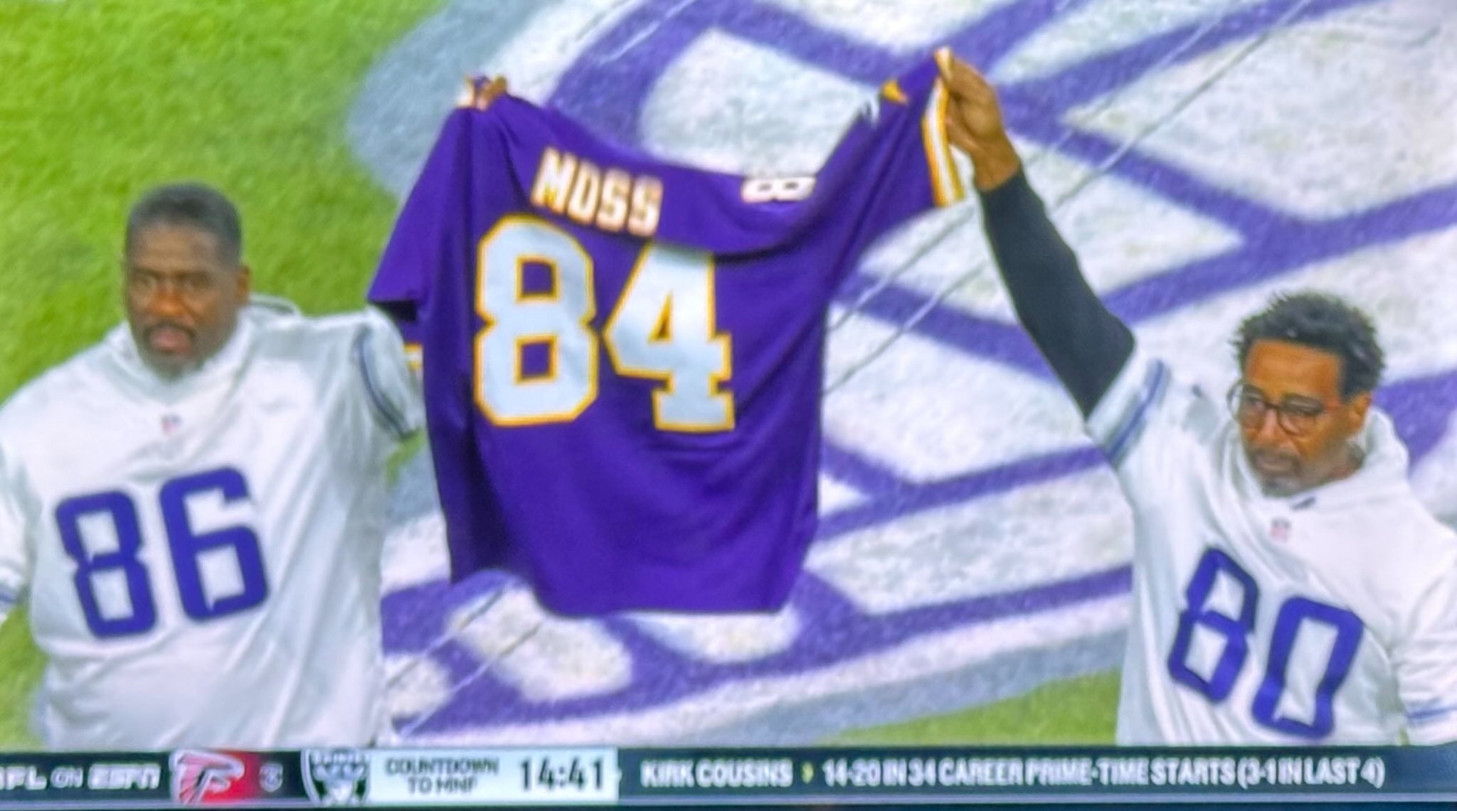 Former Minnesota Vikings wide receivers Jake Reed (86) and Pro Football Hall of Famer Cris Carter (80) hold up Randy Moss' jersey to show support after his cancer diagnosis.