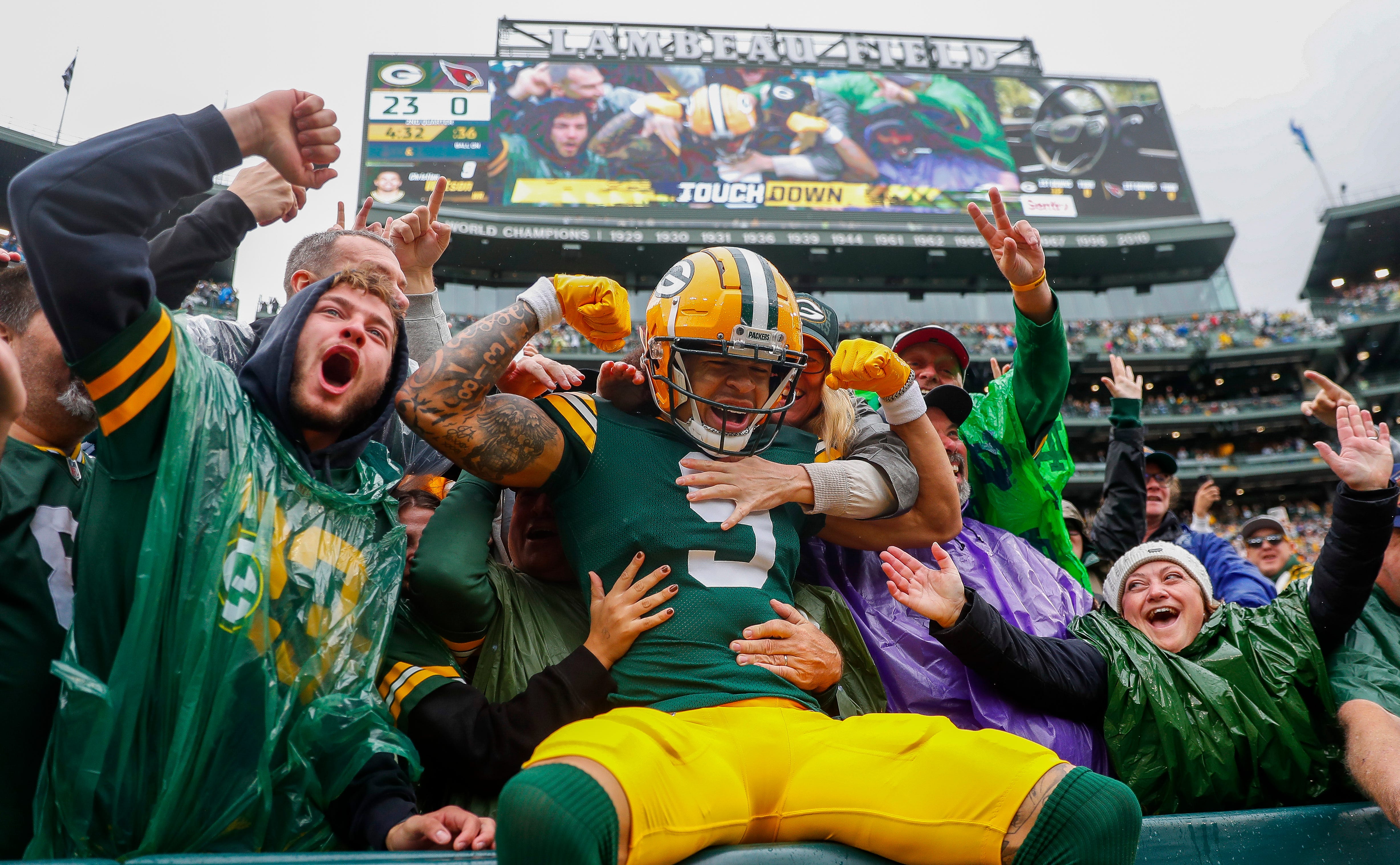 Green Bay Packers wide receiver Christian Watson (9) flexes as he does a “Lambeau Leap” with Packers fans after scoring a touchdown against the Arizona Cardinals on Sunday, October 13, 2024, at Lambeau Field in Green Bay, Wis. The Packers won the game, 34-13