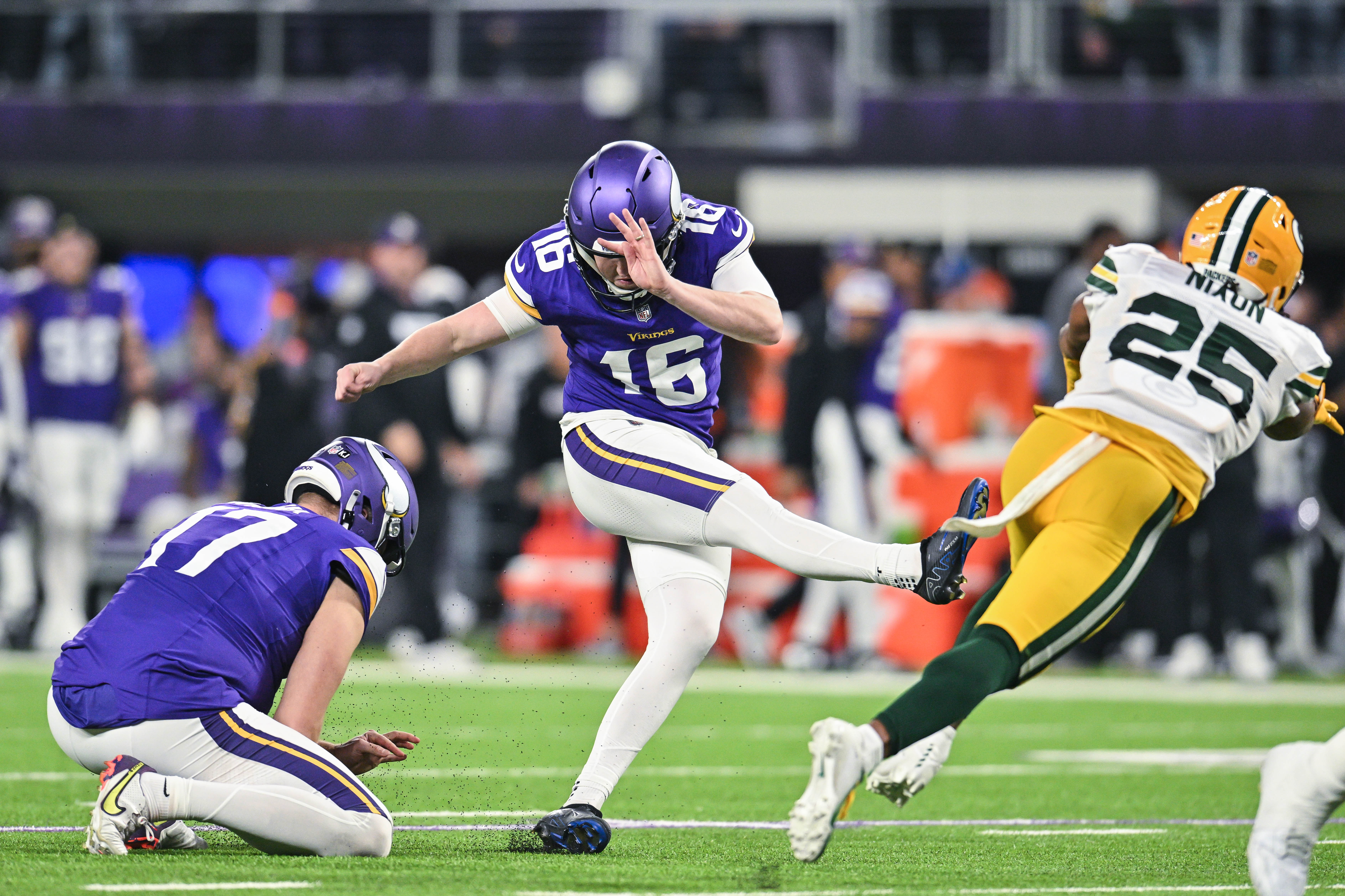 Dec 29, 2024; Minneapolis, Minnesota, USA; Minnesota Vikings place kicker Will Reichard (16) kicks an extra point as punter Ryan Wright (17) holds and Green Bay Packers cornerback Keisean Nixon (25) goes for the block during the third quarter at U.S. Bank Stadium.