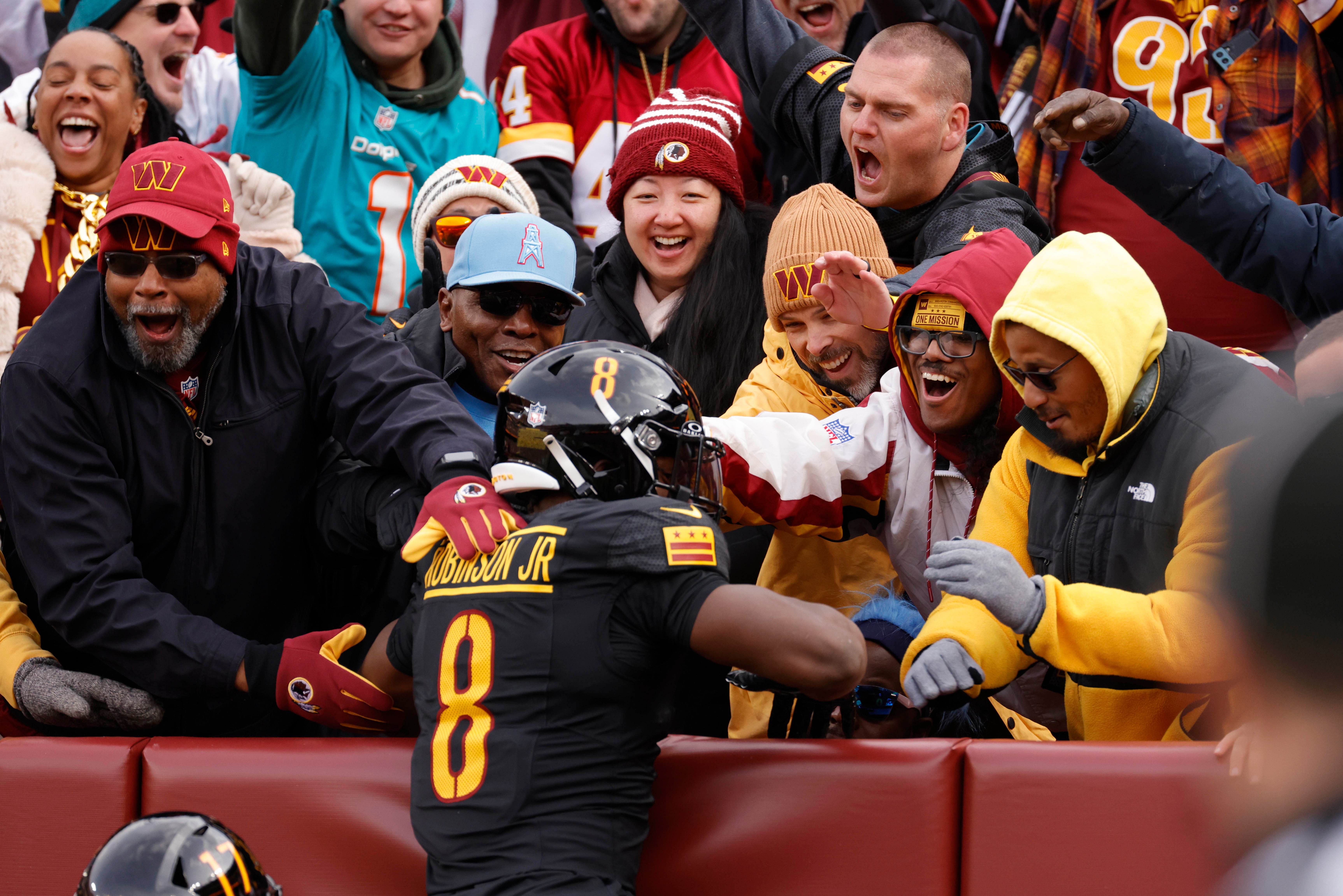 Dec 1, 2024; Landover, Maryland, USA; Fan celebrate with Washington Commanders running back Brian Robinson Jr. (8) from the stands after scoring a touchdown during the first half against the Tennessee Titans at Northwest Stadium.
