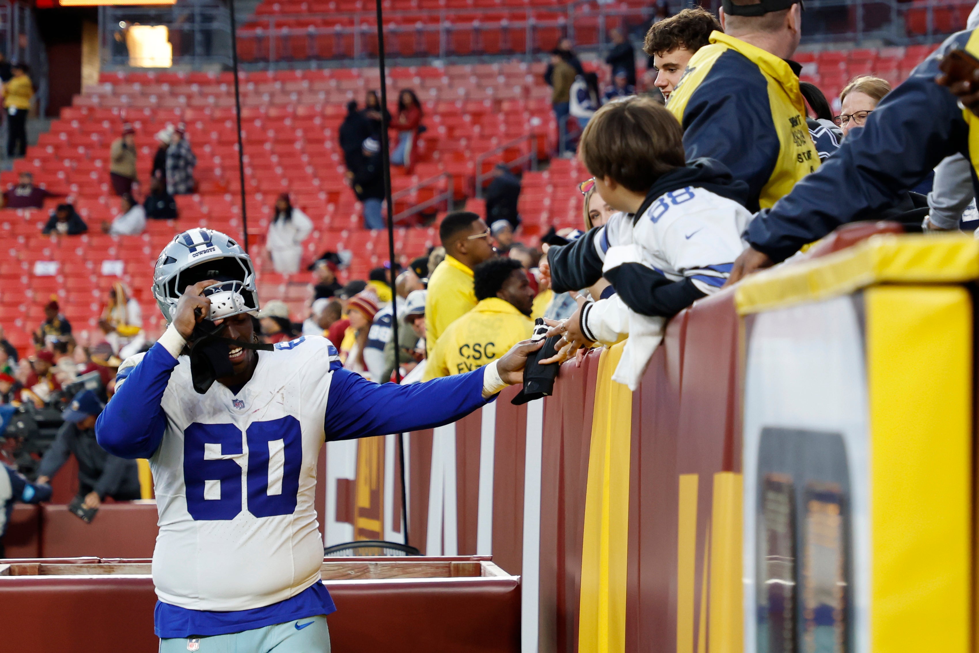 Dallas Cowboys offensive tackle Tyler Guyton (60) hands his glove to a young fan while leaving the field after the Cowboys' game against the Washington Commanders at Northwest Stadium.