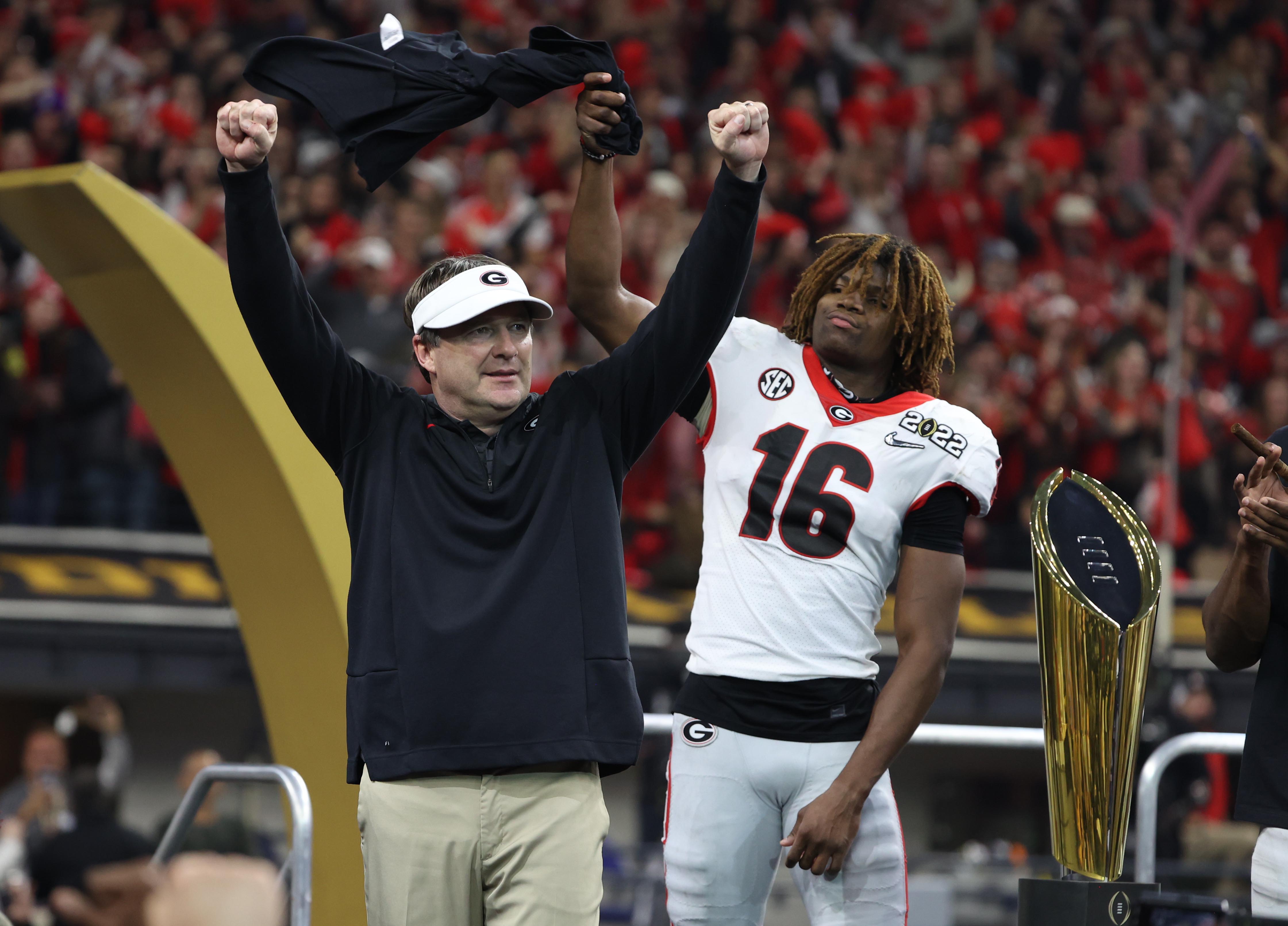 Georgia Bulldogs head coach Kirby Smart celebrates with defensive back Lewis Cine (16) on stage after defeating the Alabama Crimson Tide during the 2022 CFP college football national championship game.