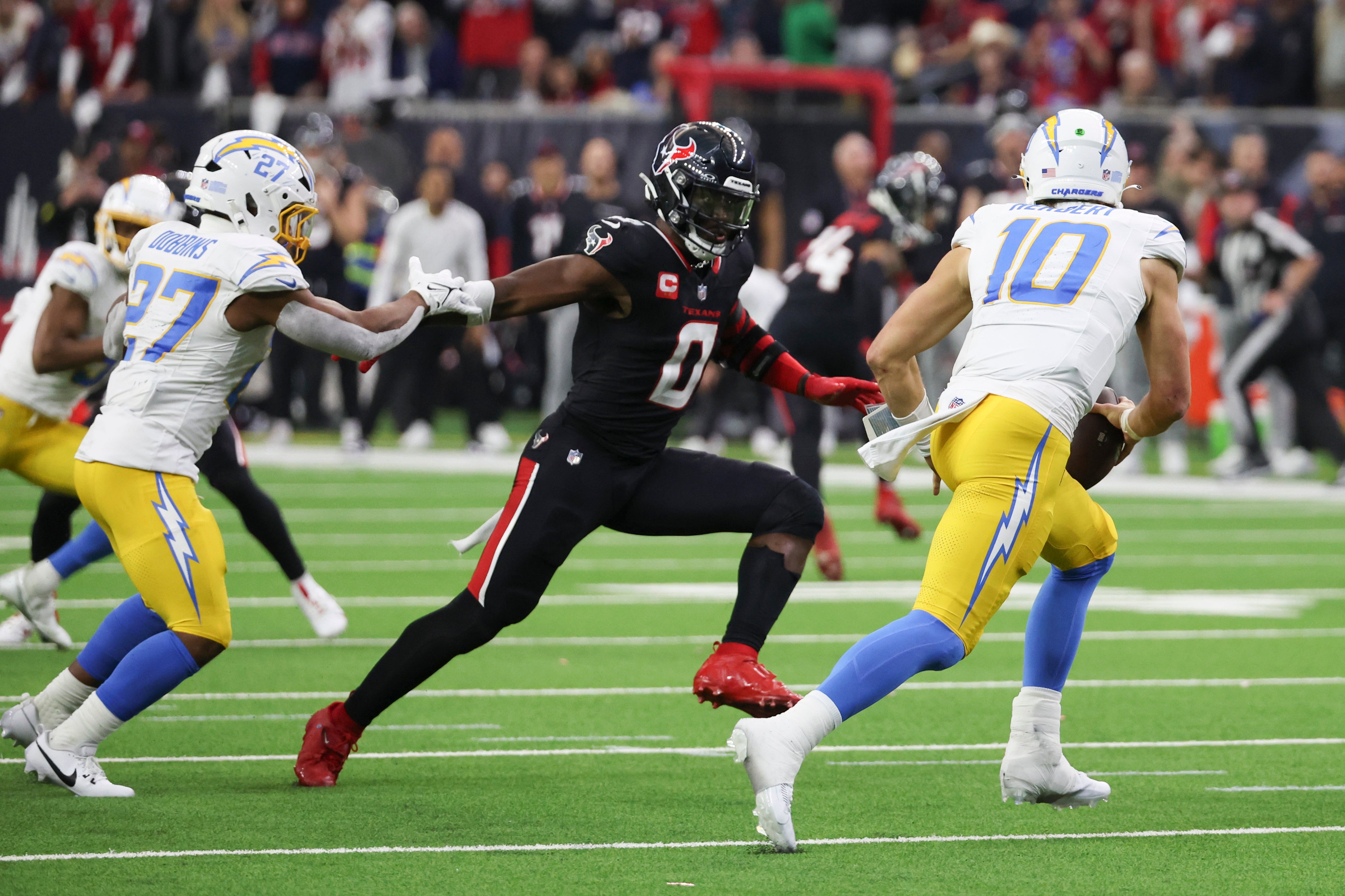 Los Angeles Chargers quarterback Justin Herbert (10) scrambles from Houston Texans linebacker Azeez Al-Shaair (0) in the second quarter in an AFC wild card game at NRG Stadium.