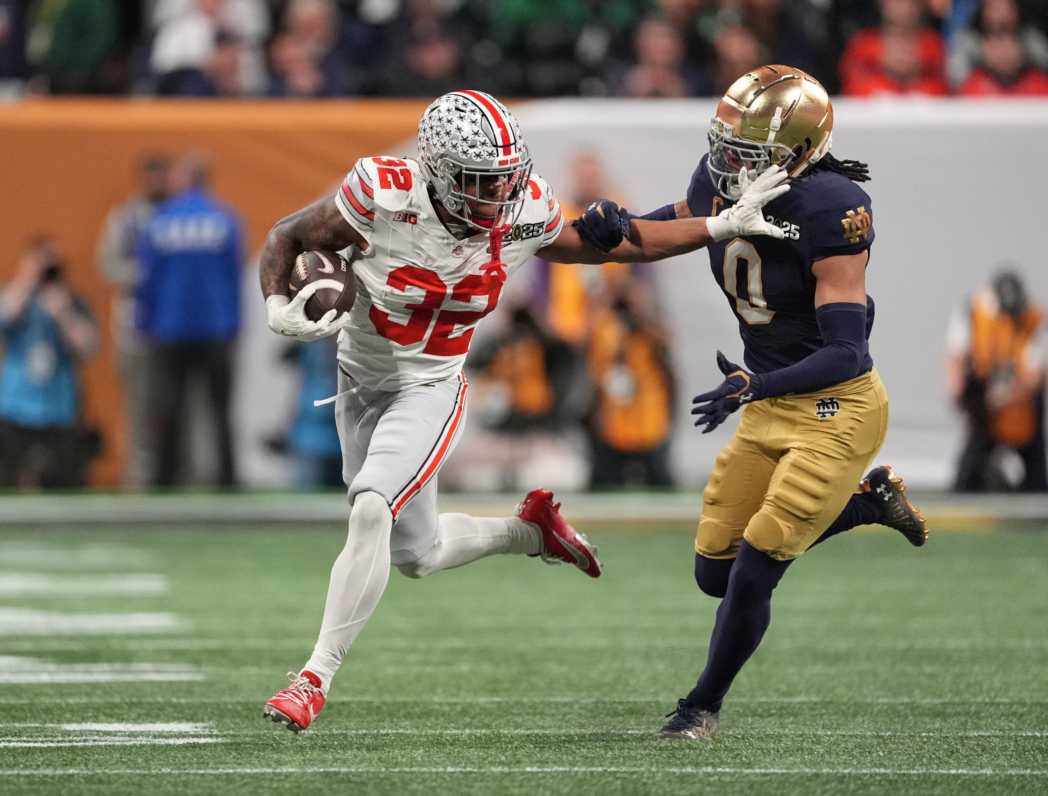 Jan 20, 2025; Atlanta, GA, USA; Ohio State Buckeyes running back TreVeyon Henderson (32) stiff arms Notre Dame Fighting Irish safety Xavier Watts (0) in the first half in the CFP National Championship college football game at Mercedes-Benz Stadium.