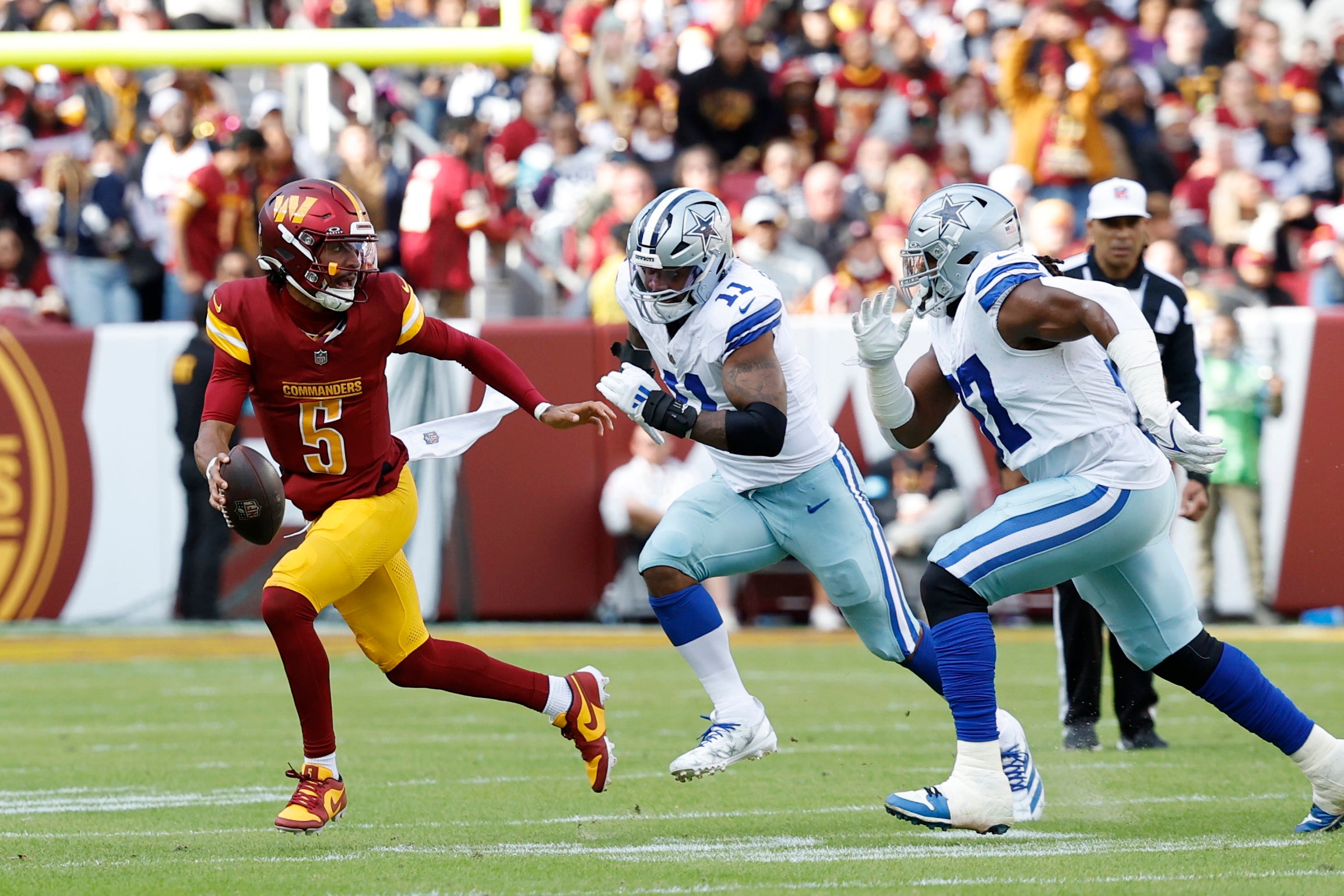 Washington Commanders quarterback Jayden Daniels (5) scrambles from Dallas Cowboys linebacker Micah Parsons (11) and Cowboys defensive tackle Osa Odighizuwa (97) at Northwest Stadium.