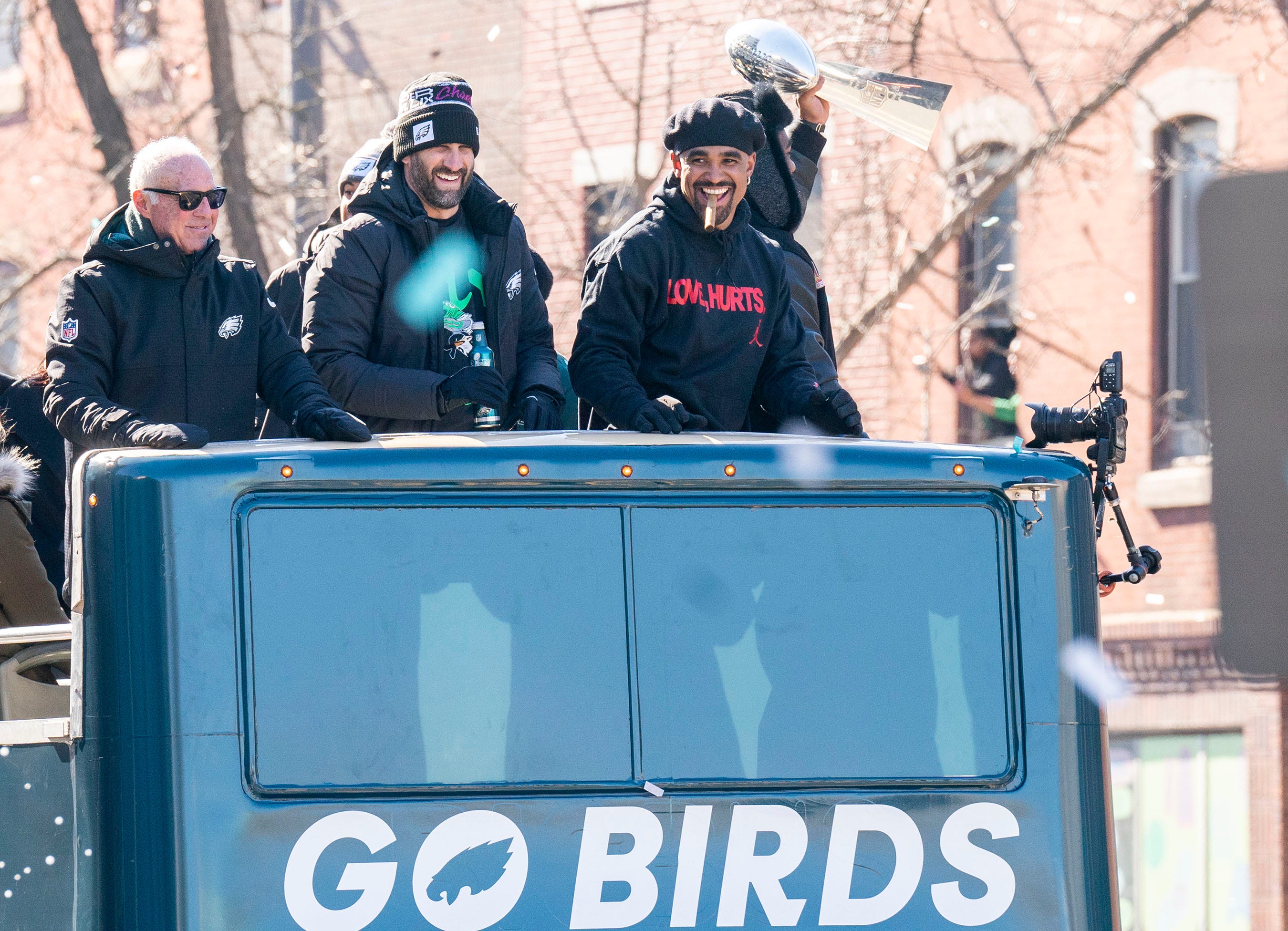 Philadelphia Eagles owner Jeffrey Lurie, left, joins head coach Nick Sirianni and quarterback Jalen Hurts atop one of the team buses during the Super Bowl 59 victory parade along South Broad Street.