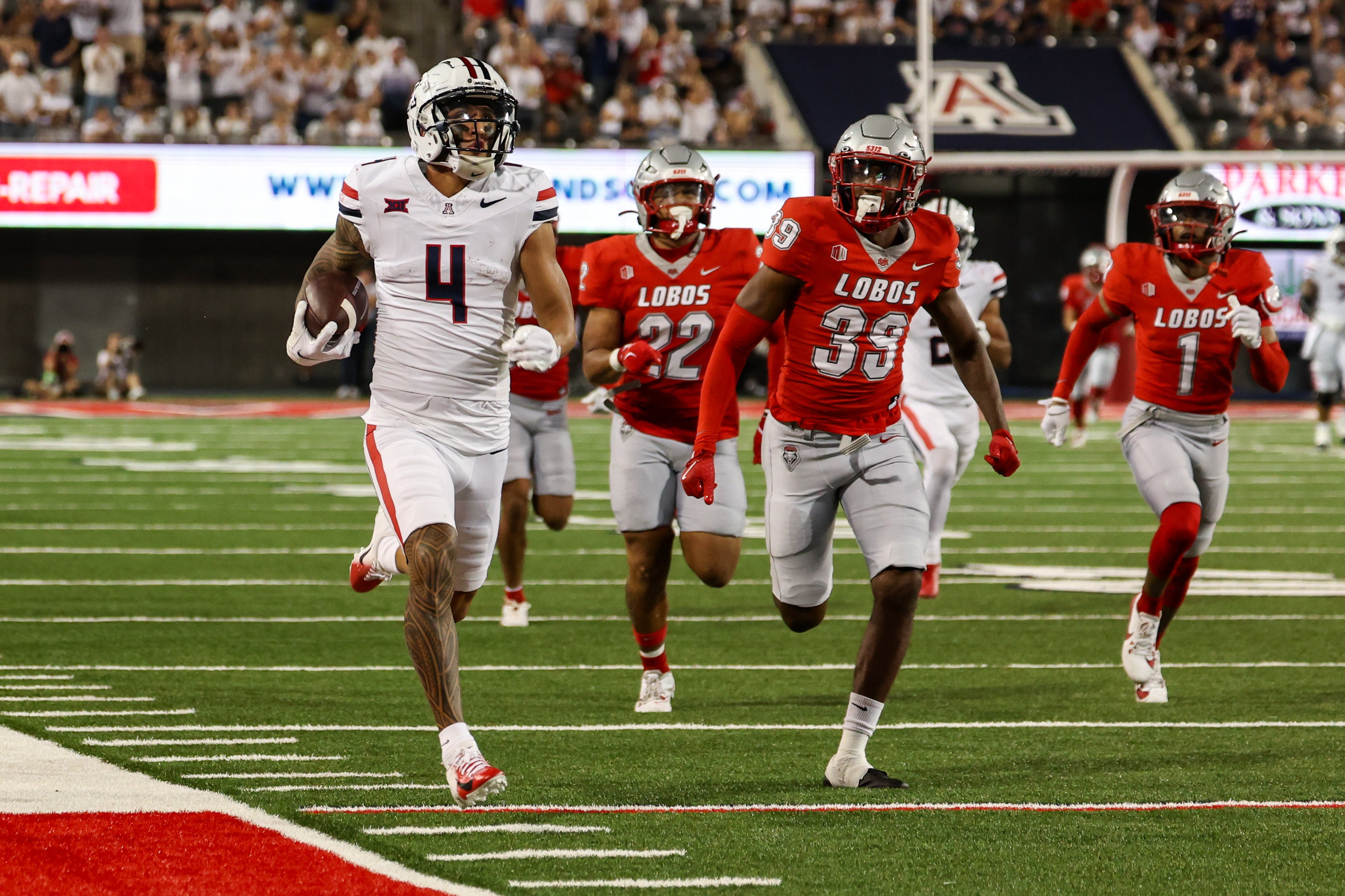 Arizona Wildcats wide receiver Tetairoa McMillan (4) runs the ball for a touchdown while being cased by New Mexico Lobos safety Dominic Tatum (39) during second quarter at Arizona Stadium.