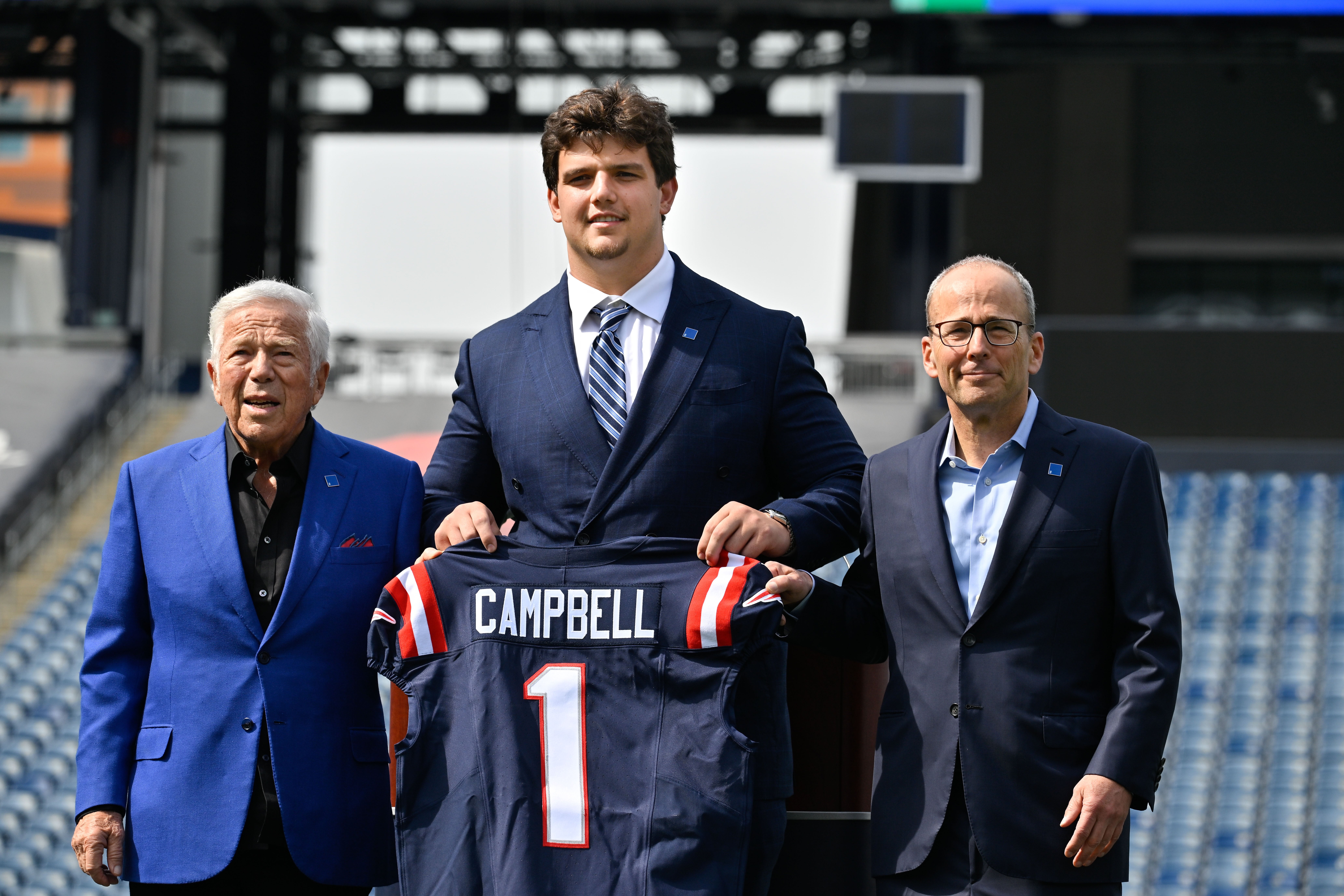 Apr 25, 2025; Foxborough, MA, USA; New England Patriots first round draft pick Will Campbell is presented with a ceremonial first round jersey by team owner Robert Kraft (l) and team president Jonathan Kraft (r) at a press conference on the game field at Gillette Stadium.