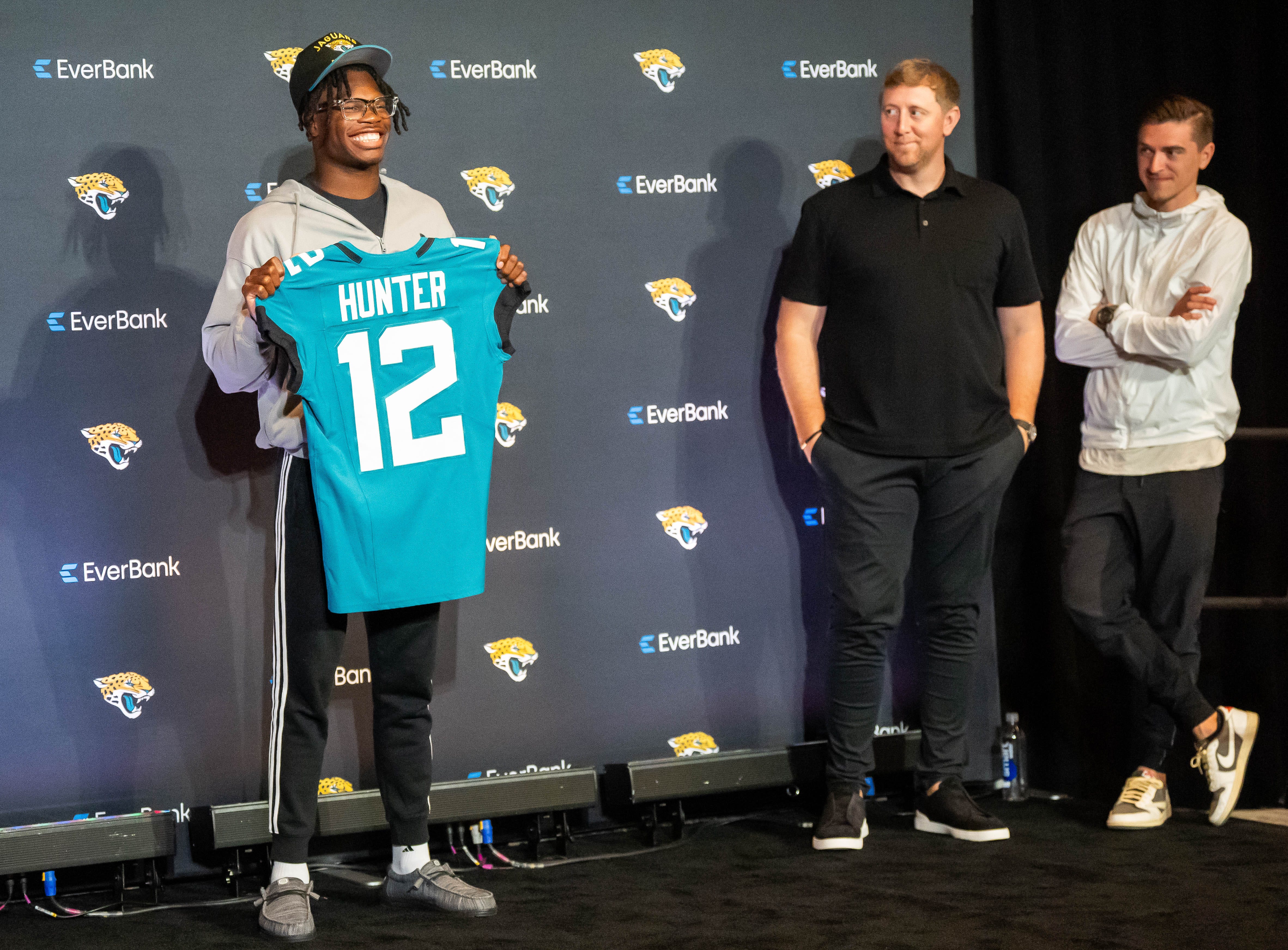 Jacksonville Jaguars wide receiver and defensive back Travis Hunter poses with his jersey during a press conference as head coach Liam Coen and general manager James Gladstone watch.