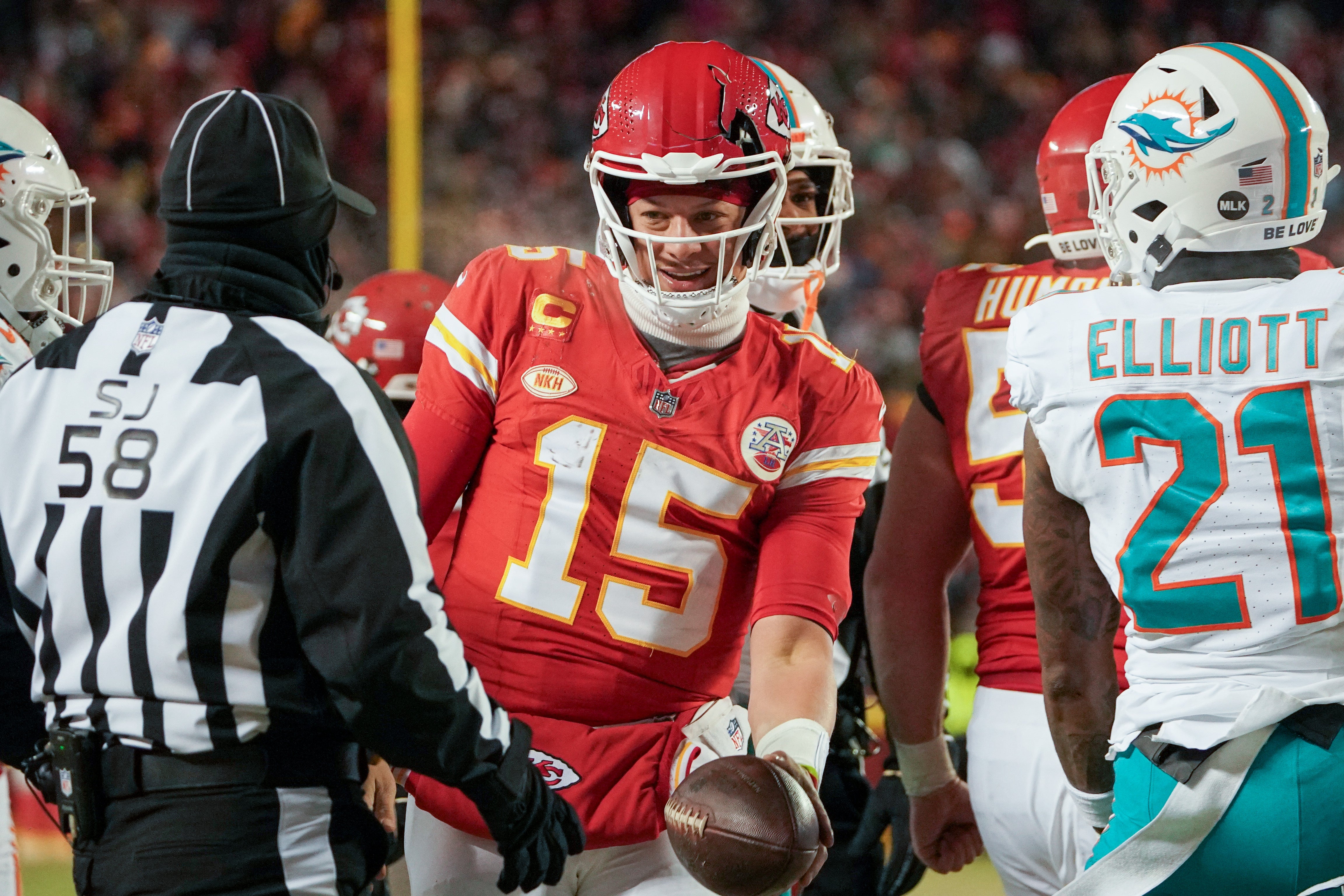 Jan 13, 2024; Kansas City, Missouri, USA; Kansas City Chiefs quarterback Patrick Mahomes (15) hands the ball to side judge Don Willard (58) after having his helmet cracked by Miami Dolphins safety DeShon Elliott (21) in a 2024 AFC wild card game at GEHA Field at Arrowhead Stadium.