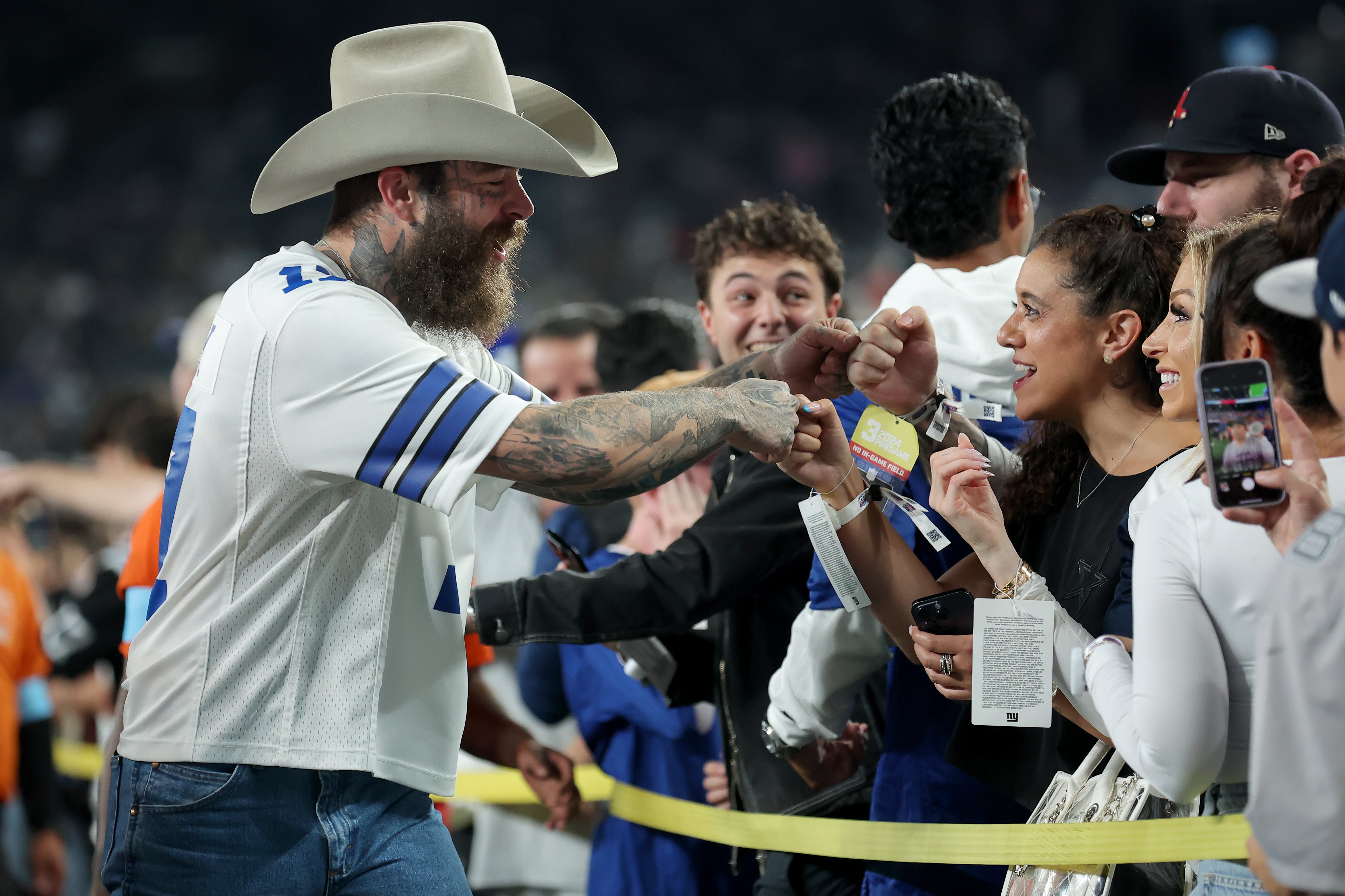 Sep 26, 2024; East Rutherford, New Jersey, USA; American recording artist Post Malone (left) fist bumps fans on the field before a game between the New York Giants and the Dallas Cowboys at MetLife Stadium.