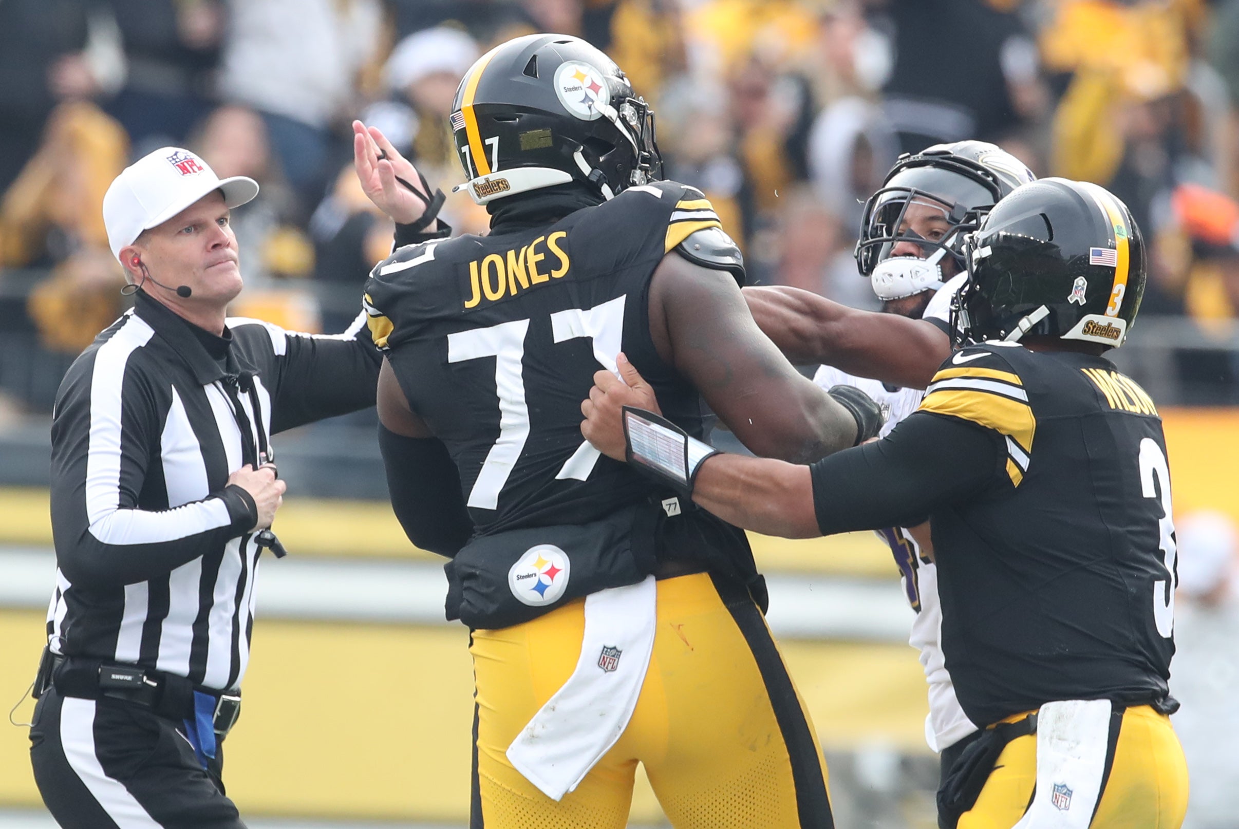 Nov 17, 2024; Pittsburgh, Pennsylvania, USA; NHL referee Clay Martin (19) and Pittsburgh Steelers quarterback Russell Wilson (3) break up a fight between Steelers offensive tackle Broderick Jones (77) and Baltimore Ravens cornerback Marlon Humphrey (44) during the second quarter at Acrisure Stadium.