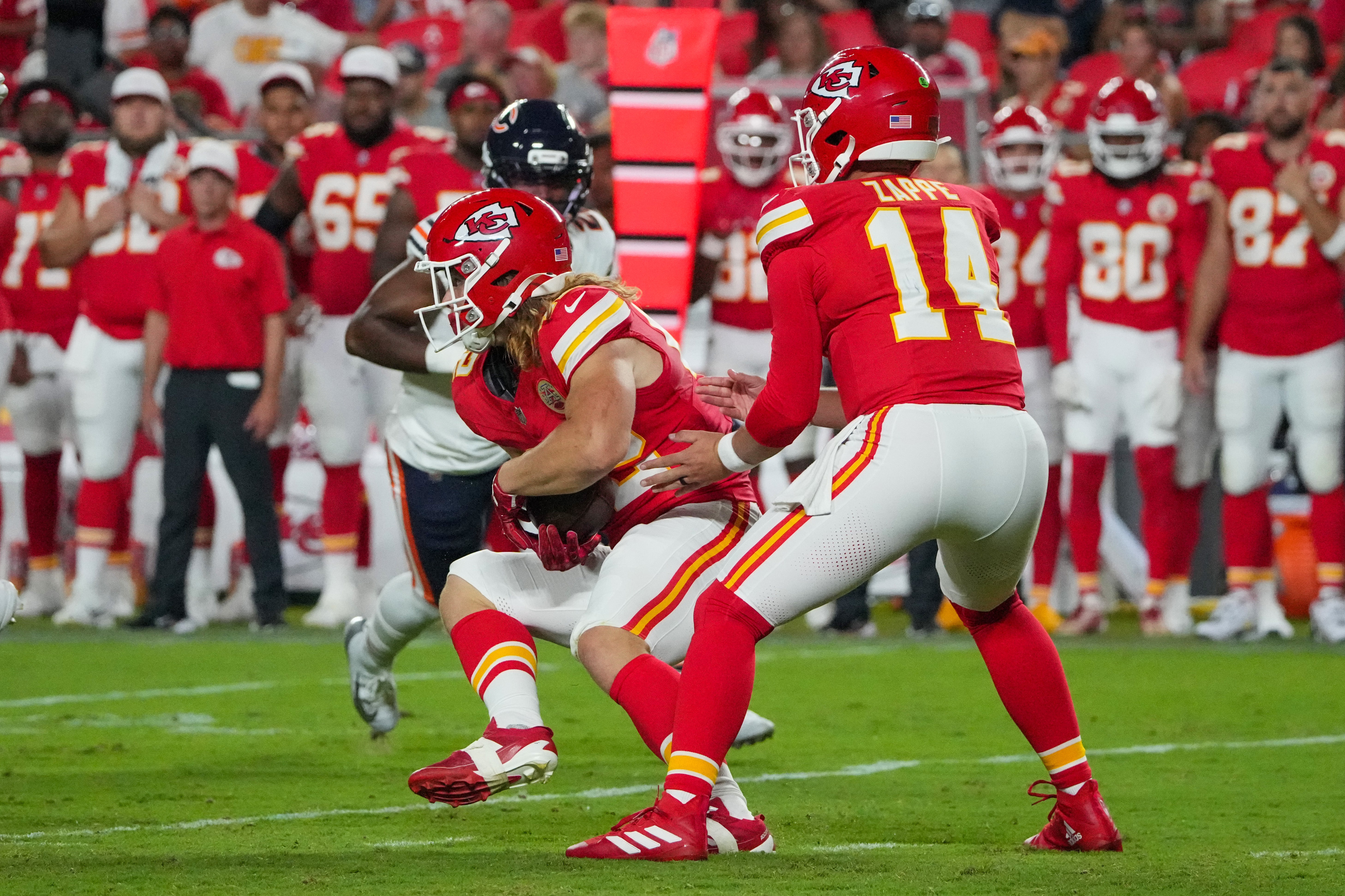 Kansas City Chiefs quarterback Bailey Zappe (14) hands off to fullback Carson Steele (42) against the Chicago Bears during the second half of the game at GEHA Field at Arrowhead Stadium.