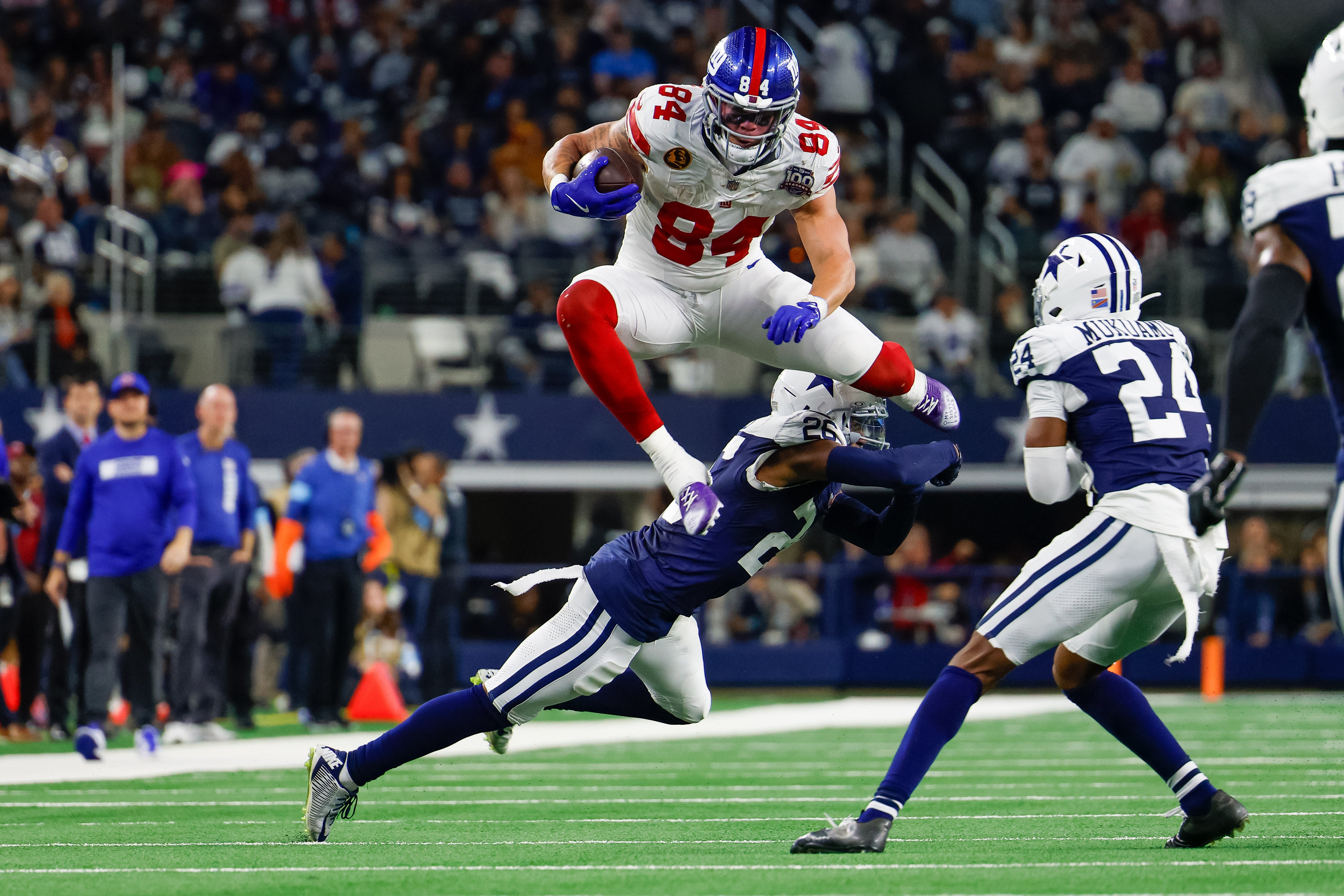 Nov 28, 2024; Arlington, Texas, USA; New York Giants tight end Theo Johnson (84) leaps over Dallas Cowboys cornerback DaRon Bland (26) during the fourth quarter at AT&T Stadium.