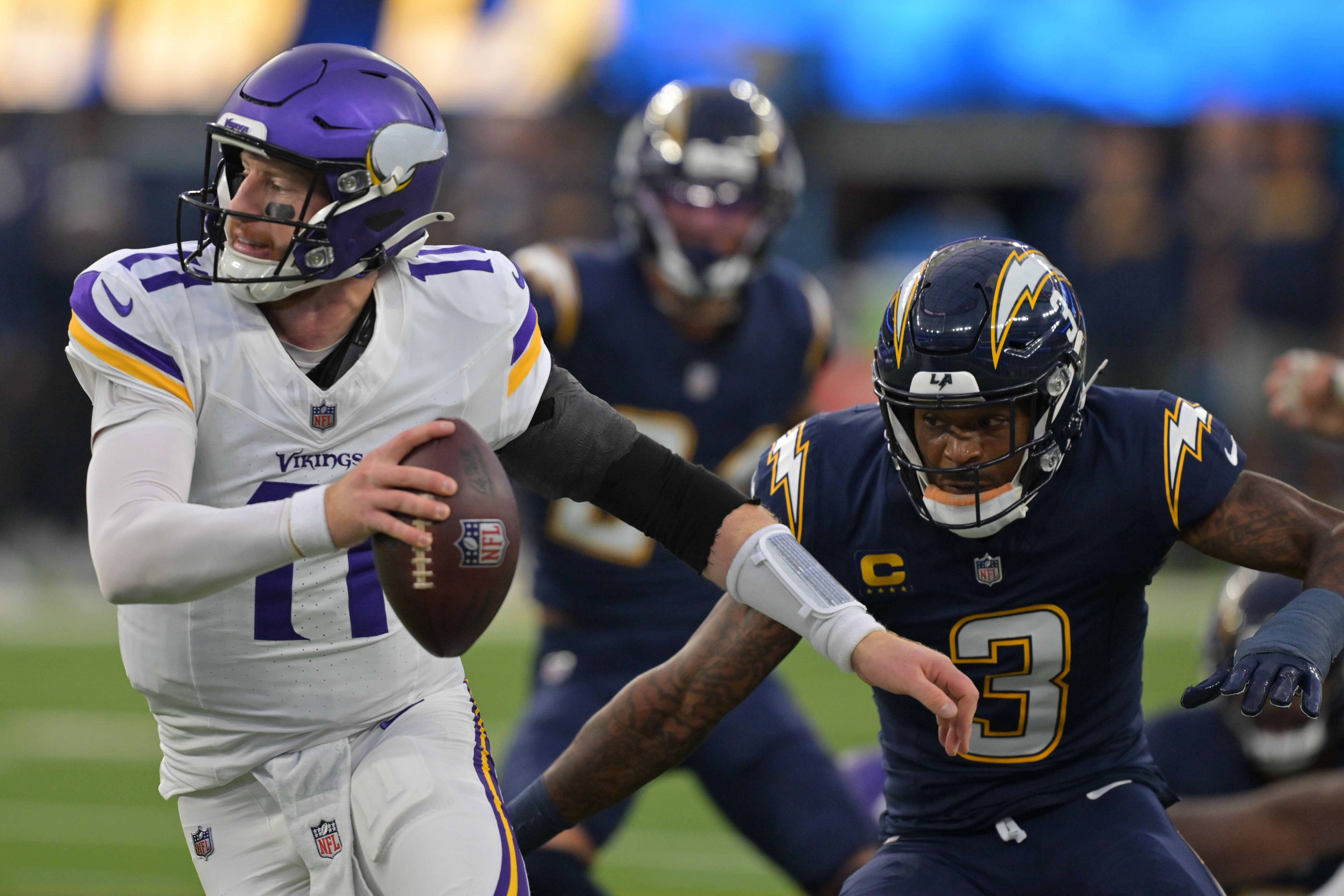 Oct 23, 2025; Inglewood, California, USA; Minnesota Vikings quarterback Carson Wentz (11) avoids the tackle of Los Angeles Chargers safety Derwin James Jr. (3) during the first half at SoFi Stadium.
