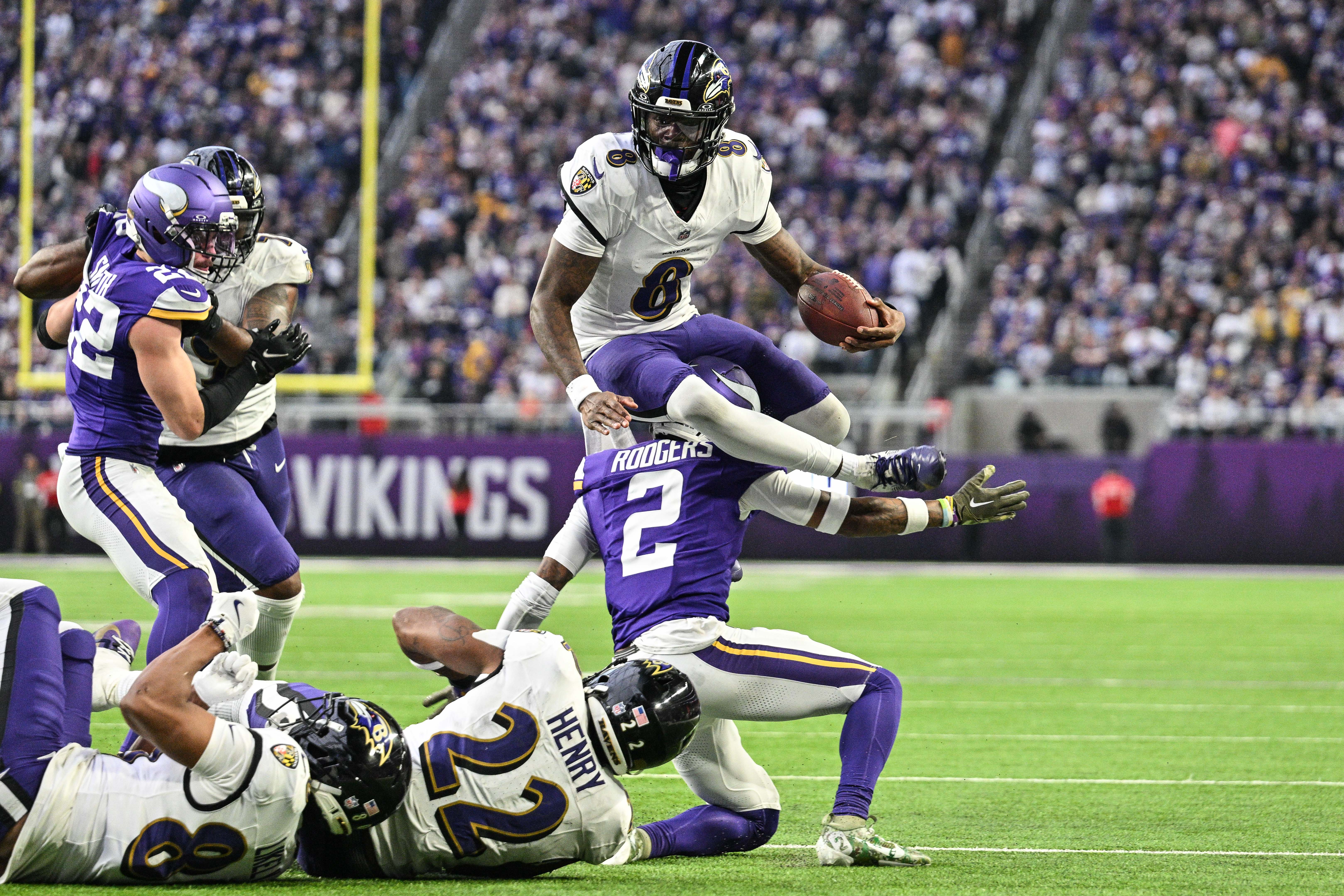 Nov 9, 2025; Minneapolis, Minnesota, USA; Baltimore Ravens quarterback Lamar Jackson (8) runs the ball as Minnesota Vikings cornerback Isaiah Rodgers (2) makes the tackle and running back Derrick Henry (22) looks on during the third quarter at U.S. Bank Stadium.