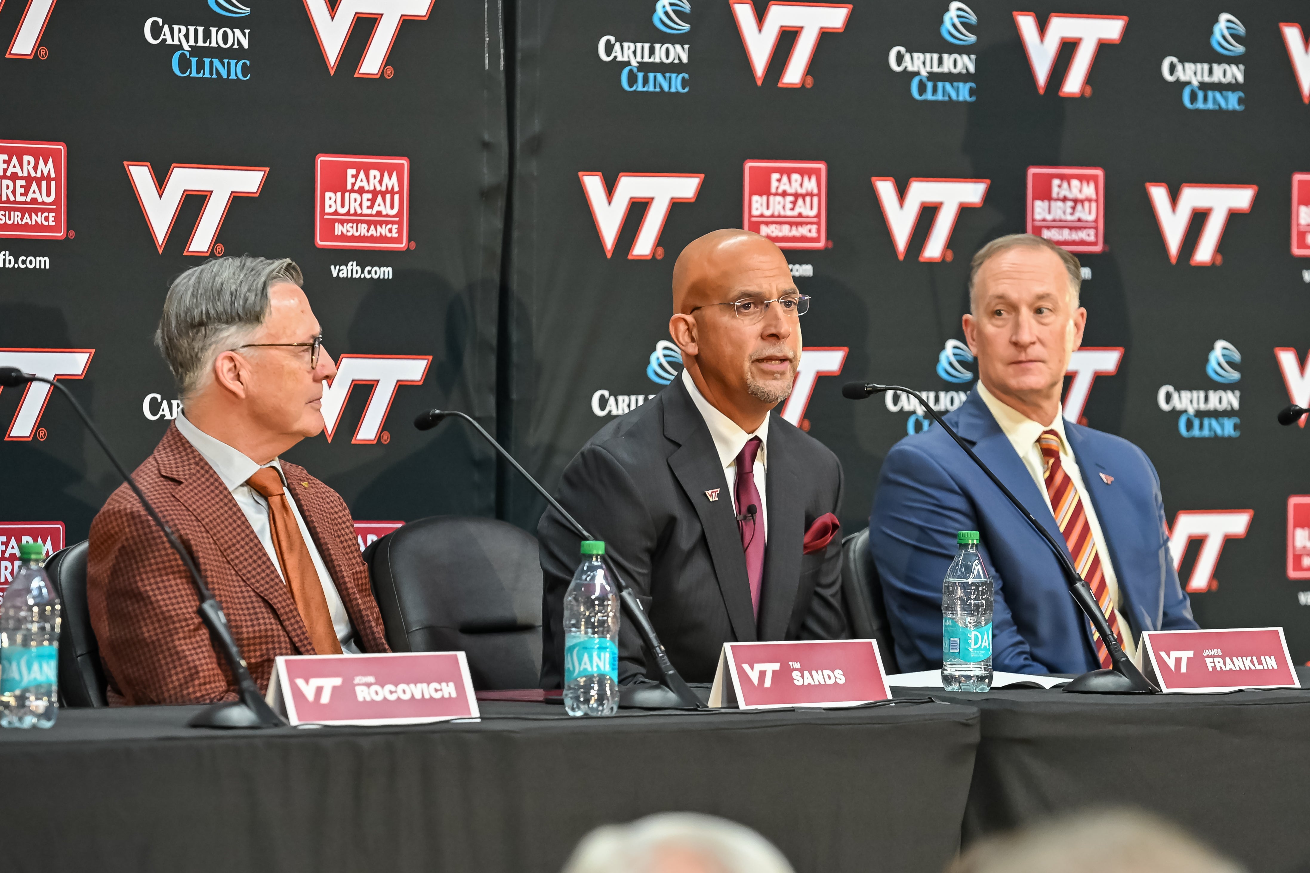 Nov 19, 2025; Blacksburg, VA, USA; Virginia Tech head coach James Franklin (center) speaks as Virginia Tech President Timothy Sands (left) and Athletic Director Whit Babcock (right) looks on at Cassell Coliseum. Mandatory Credit: Brian Bishop-Imagn Images