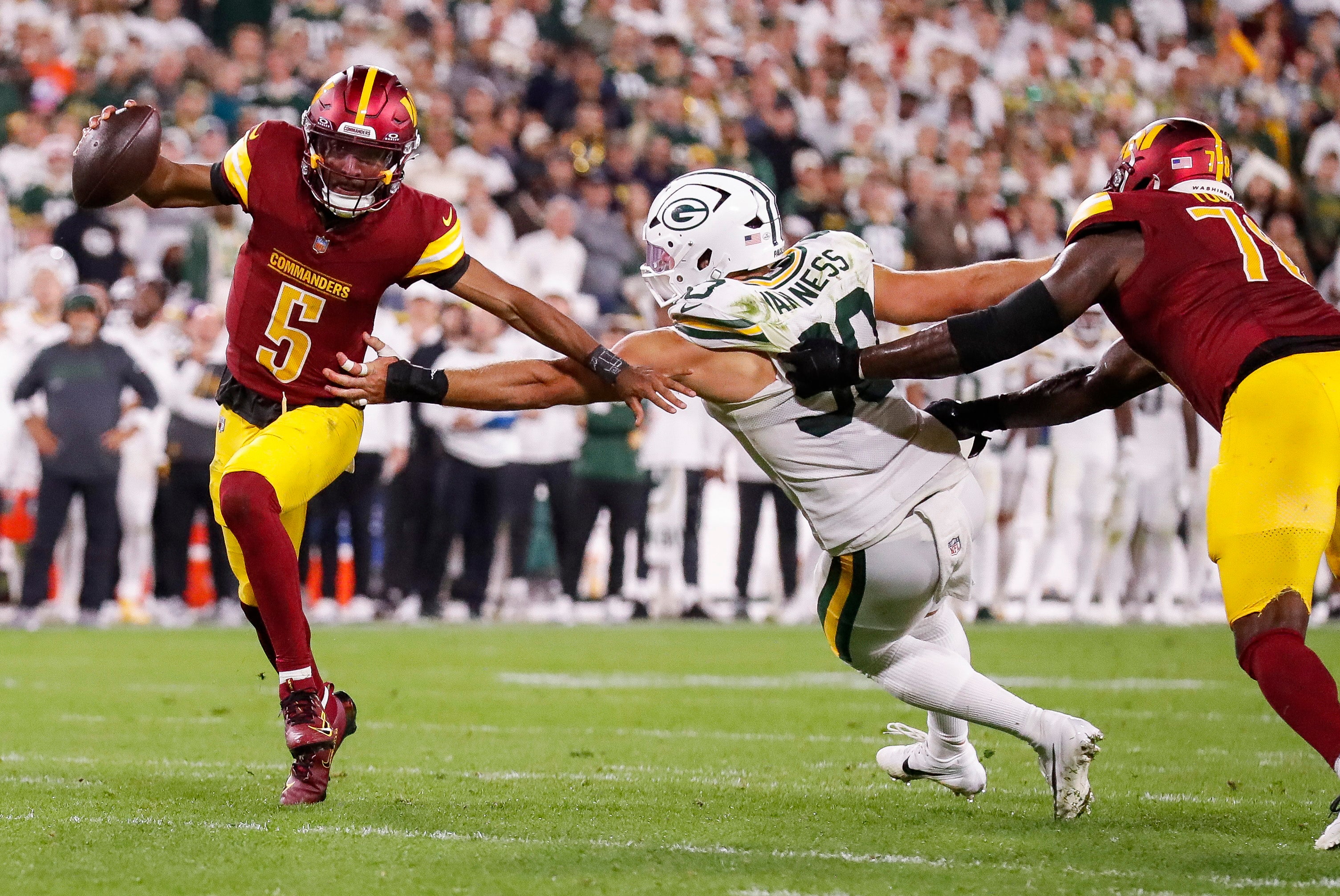 Sep 11, 2025; Green Bay, Wisconsin, USA; Washington Commanders quarterback Jayden Daniels (5) scrambles away from Green Bay Packers defensive end Lukas Van Ness (90) at Lambeau Field.