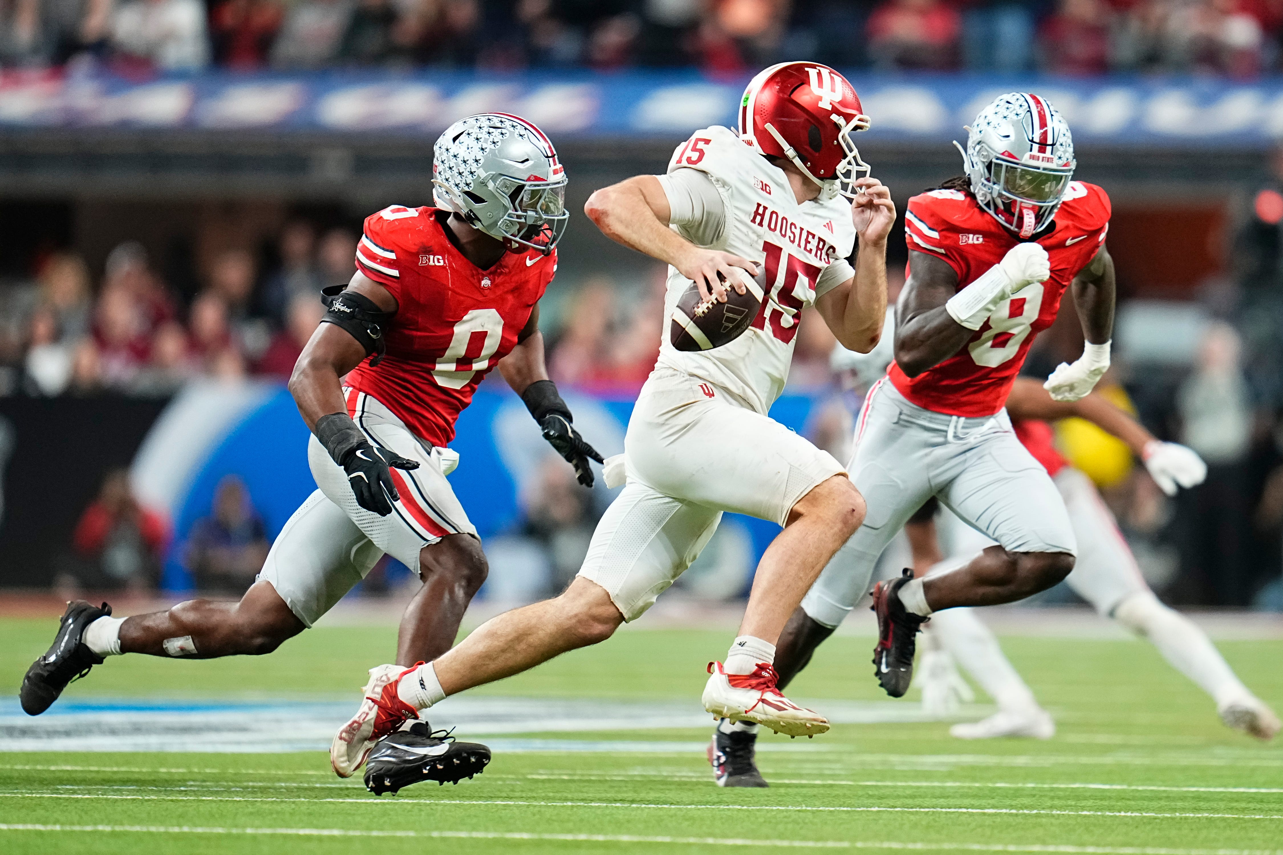 Indiana Hoosiers quarterback Fernando Mendoza (15) scrambles past Ohio State Buckeyes linebacker Sonny Styles (0) and linebacker Arvell Reese (8) during the Big Ten Conference championship game at Lucas Oil Stadium in Indianapolis on Dec. 6, 2025. Ohio State lost 13-10.