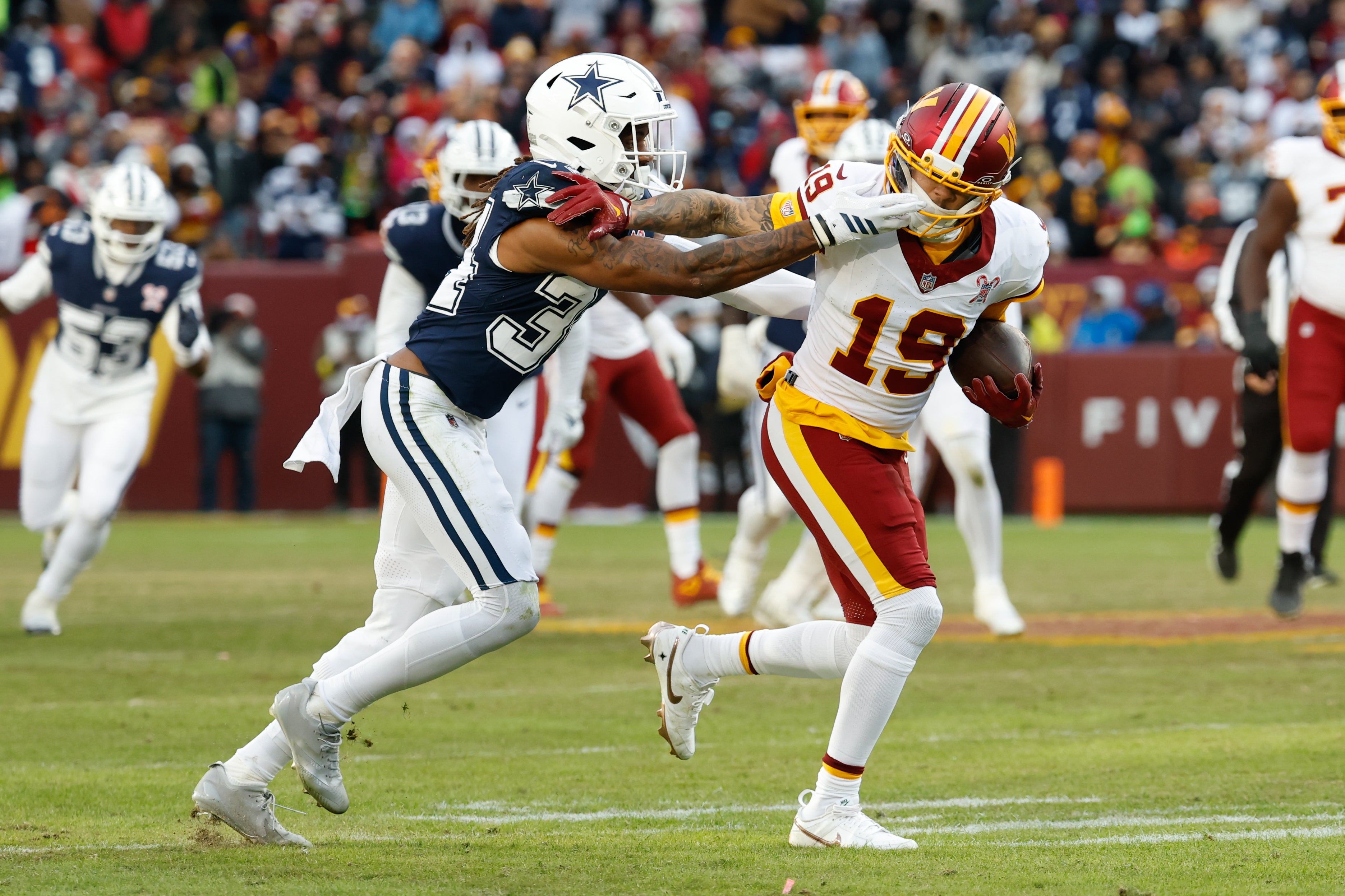 Dec 25, 2025; Landover, Maryland, USA; Washington Commanders wide receiver Chris Moore (19) carries the ball after a reception defended by Dallas Cowboys cornerback Shavon Revel Jr. (34) in the third quarter at Northwest Stadium.